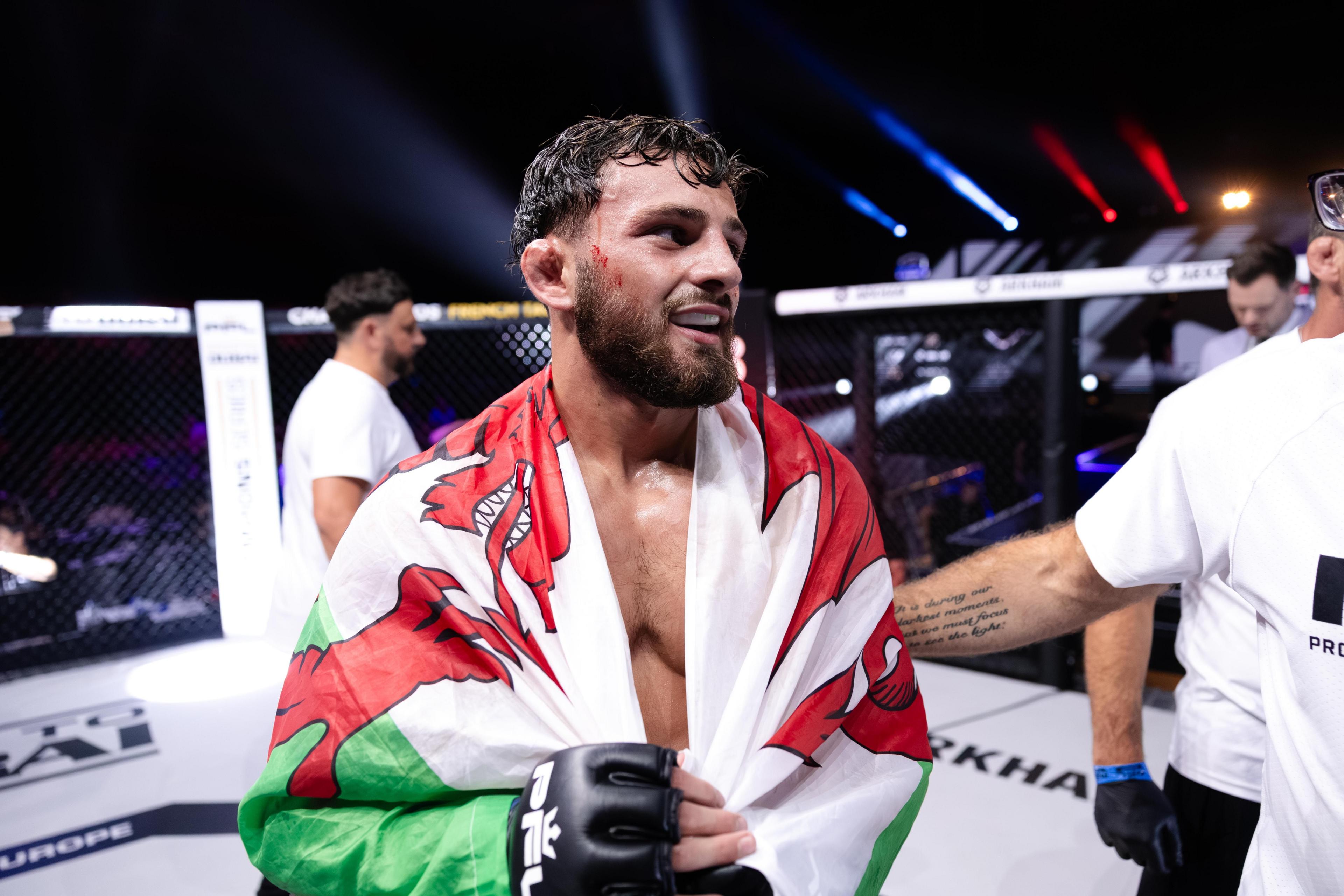 MMA fighter Levi Batchelor smiling and holding a Welsh flag over his shoulders.