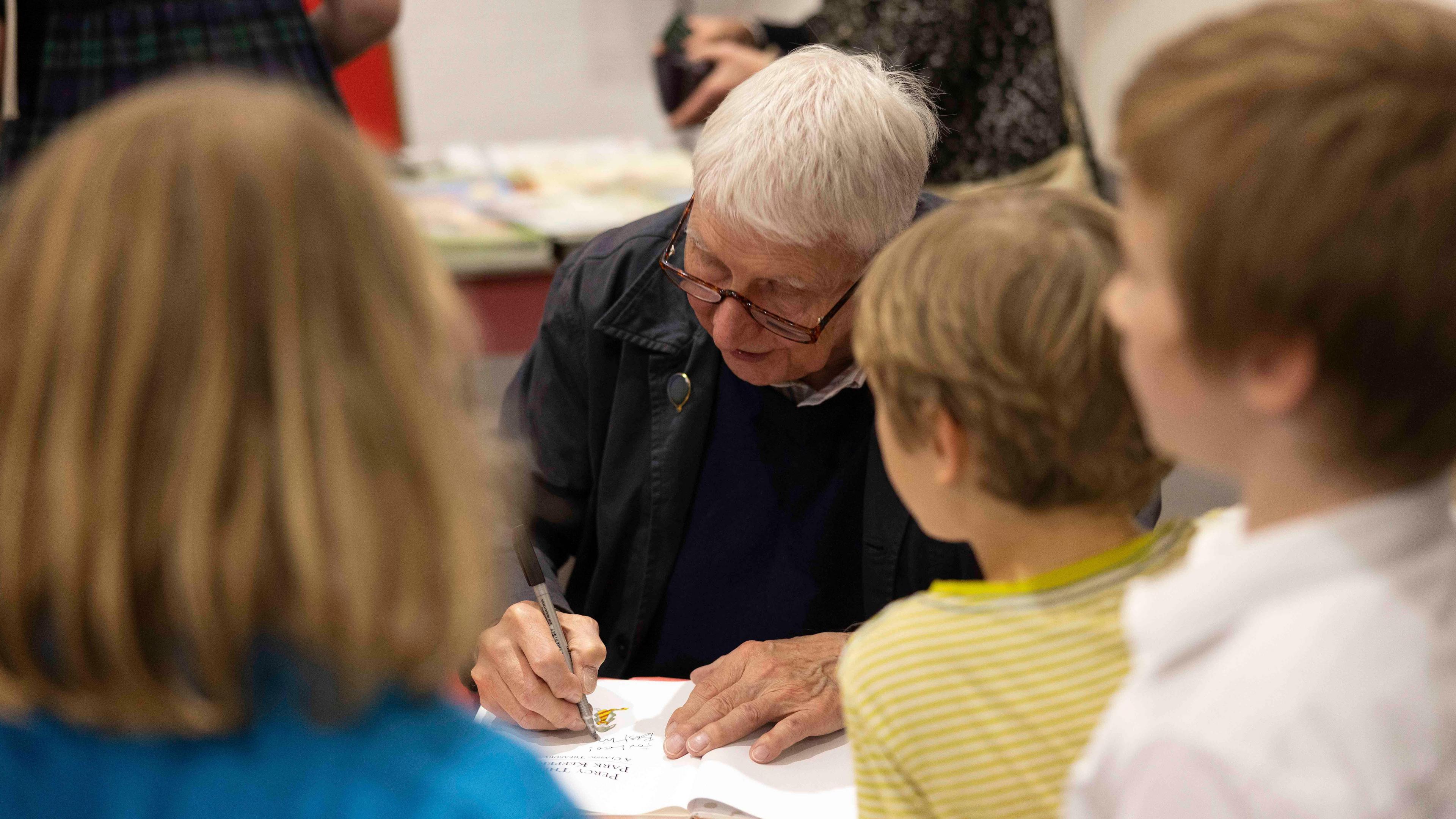 A group of children crowd around Nick Butterworth who is signing a book.