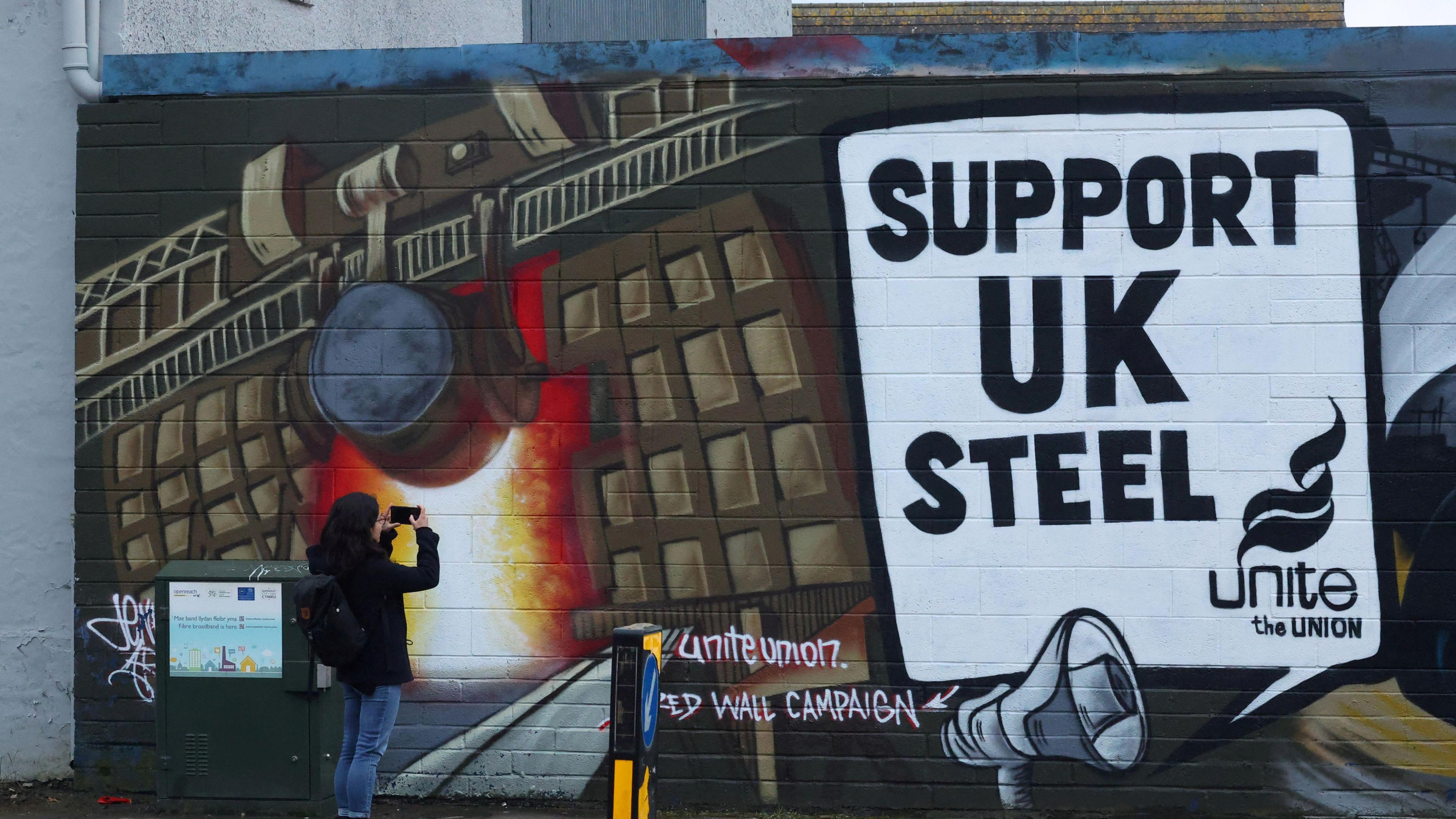 A woman photographing a mural near the Port Talbot steelworks