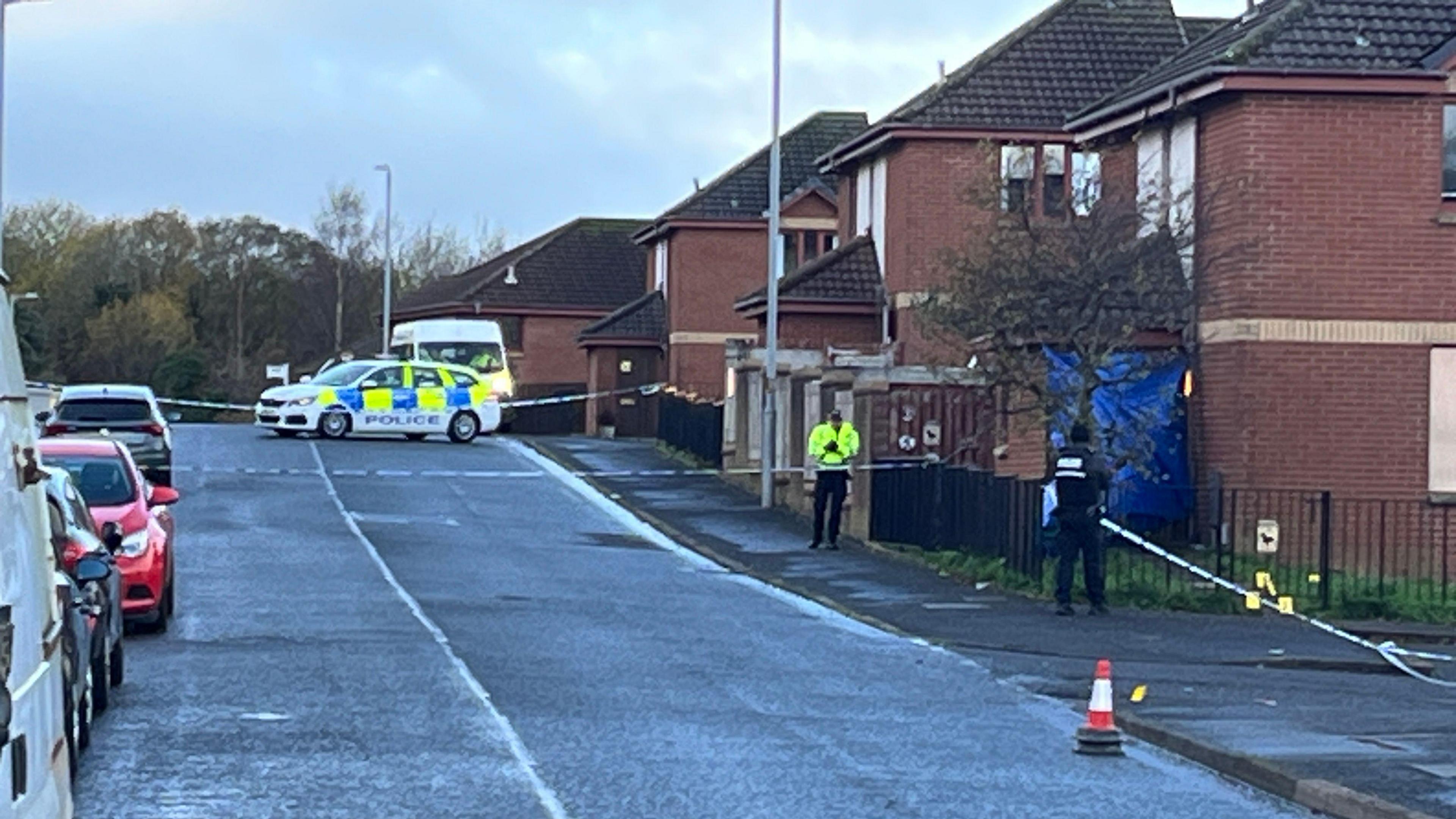 A cordoned off residential street with a police car and police van