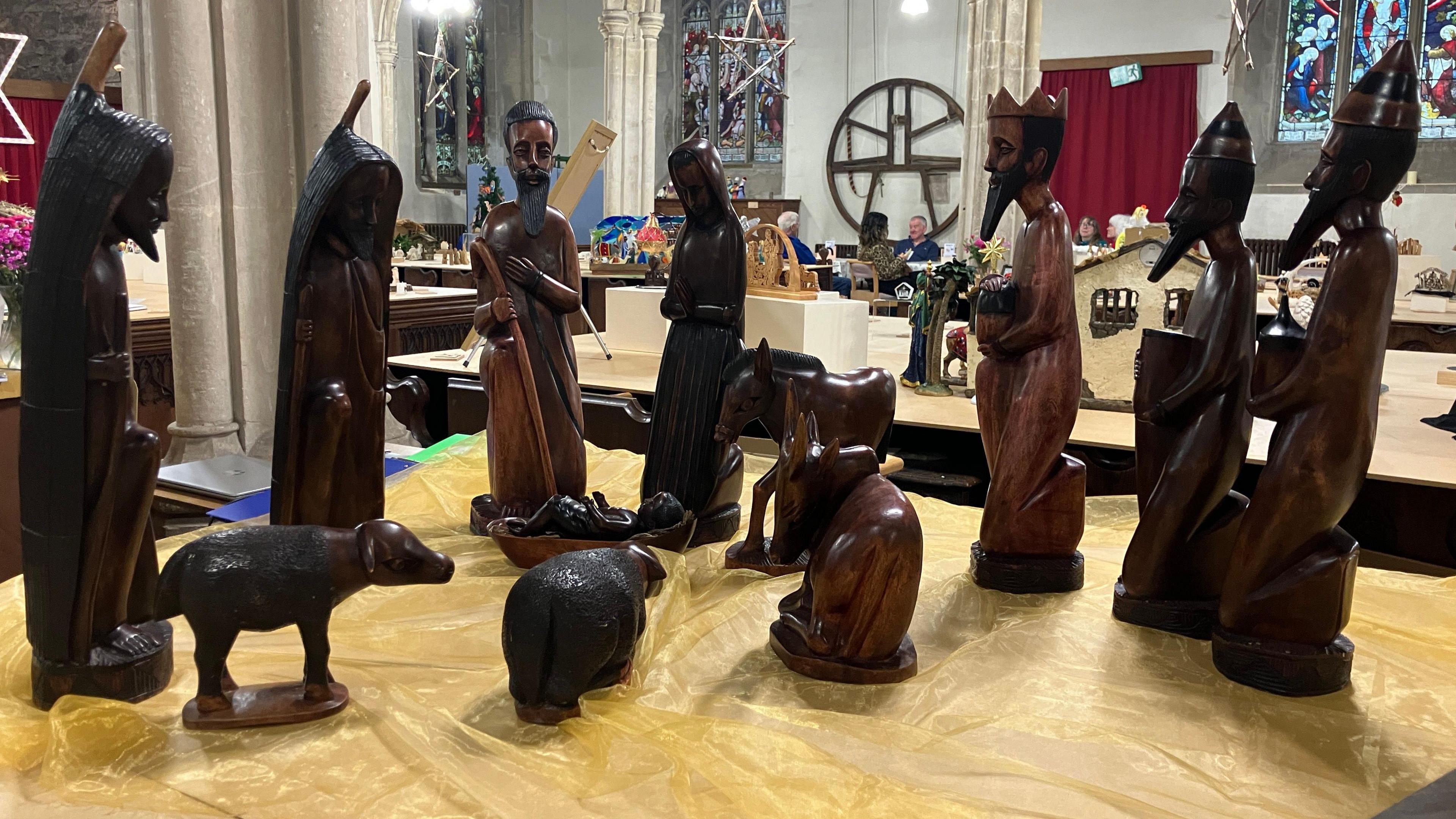 A wooden nativity scene from Rwanda. All the figures are made from a dark brown wood. They depict several people, including baby Jesus, the three wise men, and animals. 