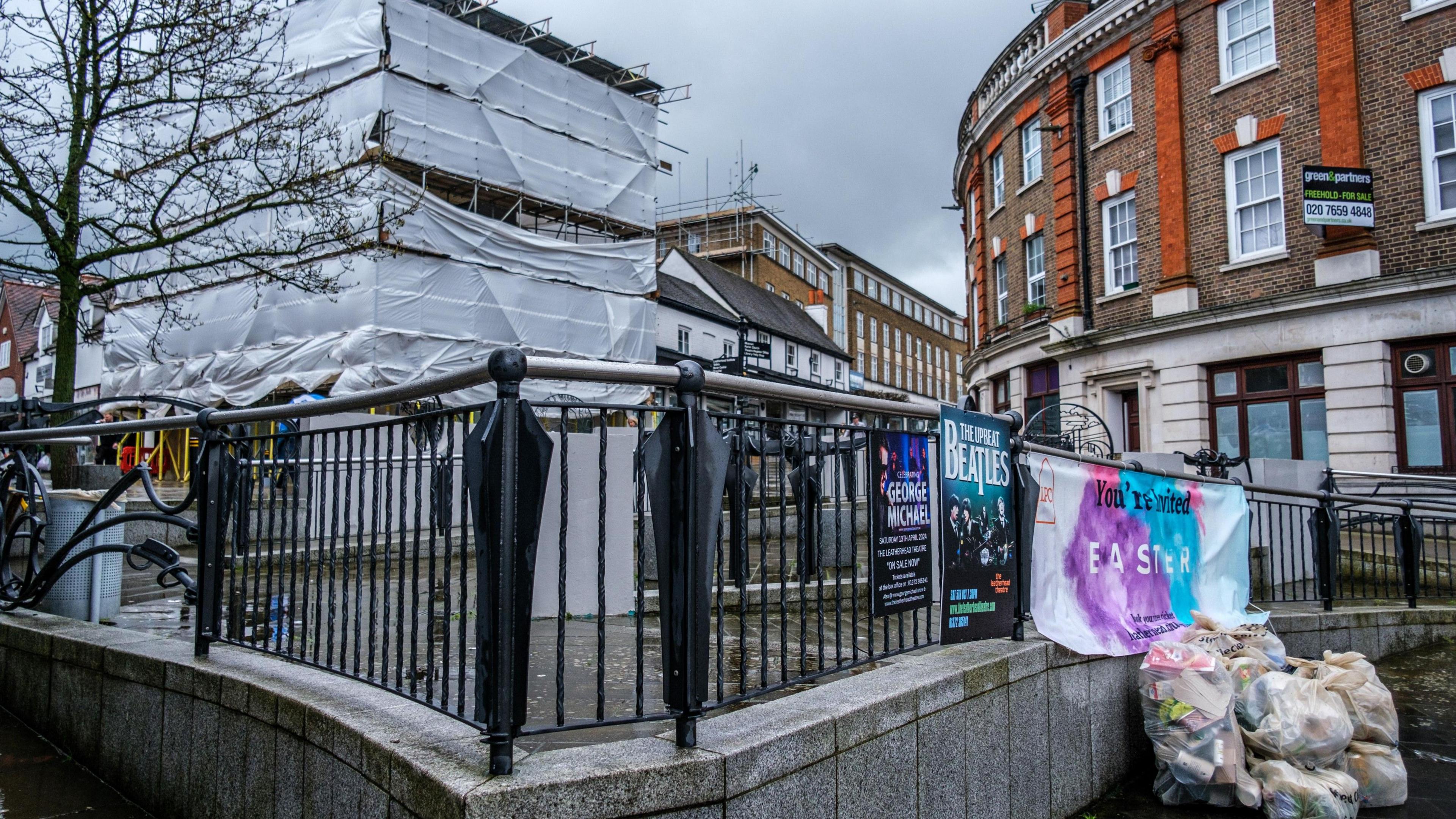 A street corner in Leatherhead, with railings, a pile of rubbish waiting to be collected and a poster advertising events at the town's theatre.