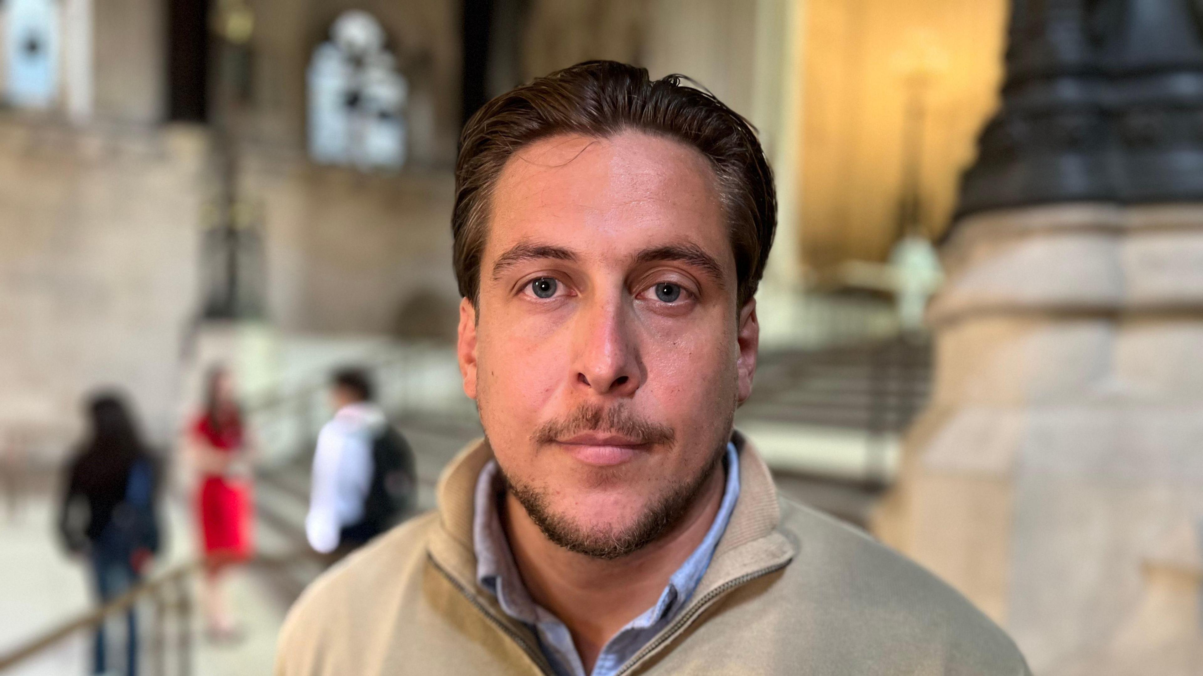 A man with slicked-back, brown hair stares into the camera.