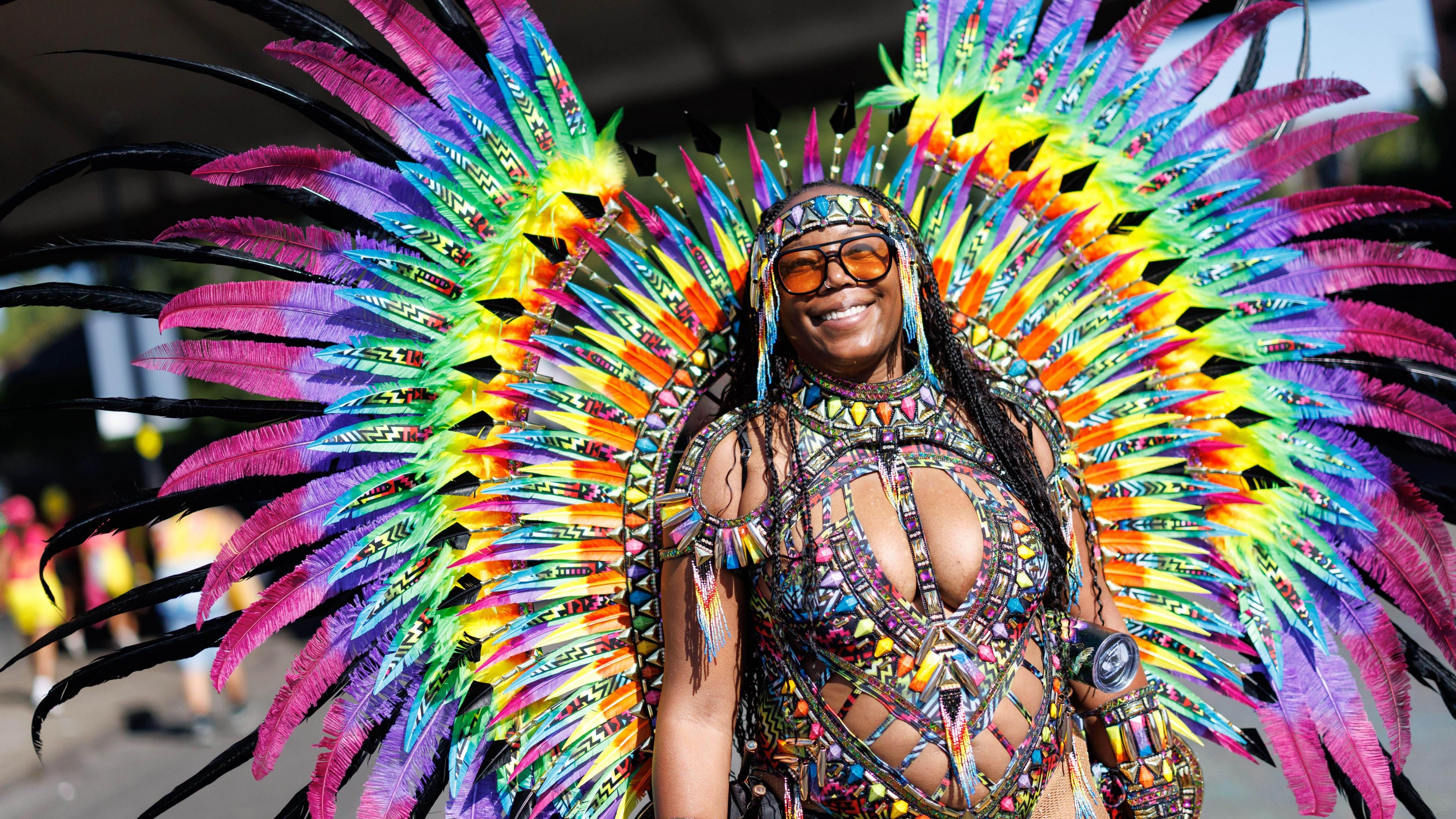 A woman wears a rainbow coloured costume with feathers fanning out behind her.