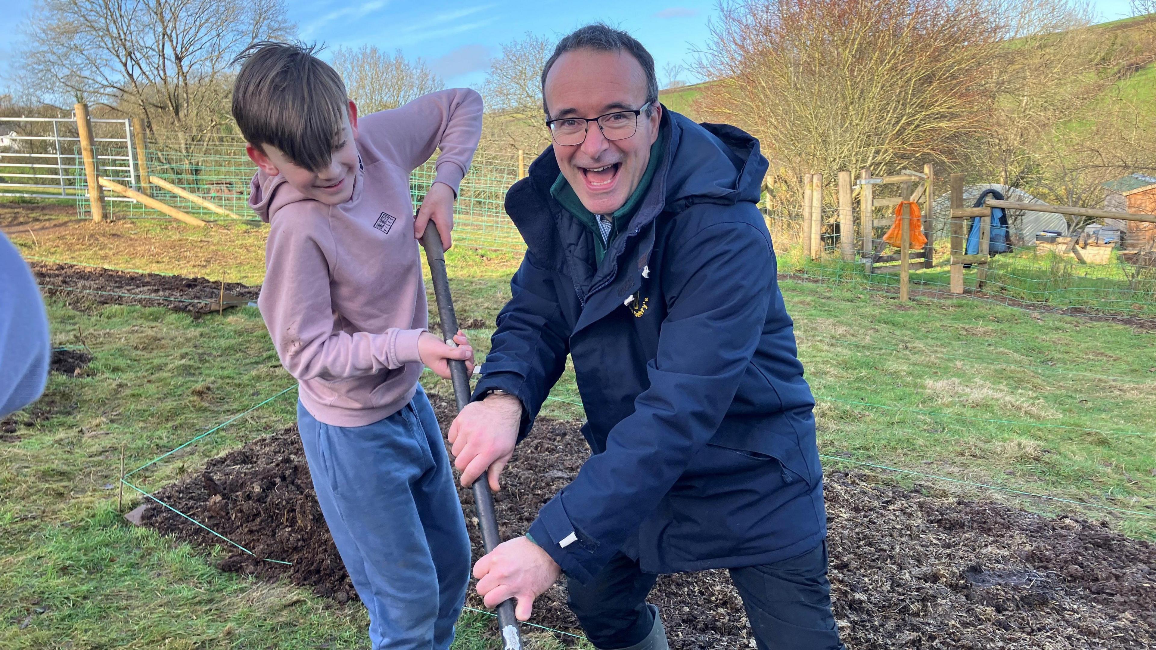 Head teacher holding rake with pupil