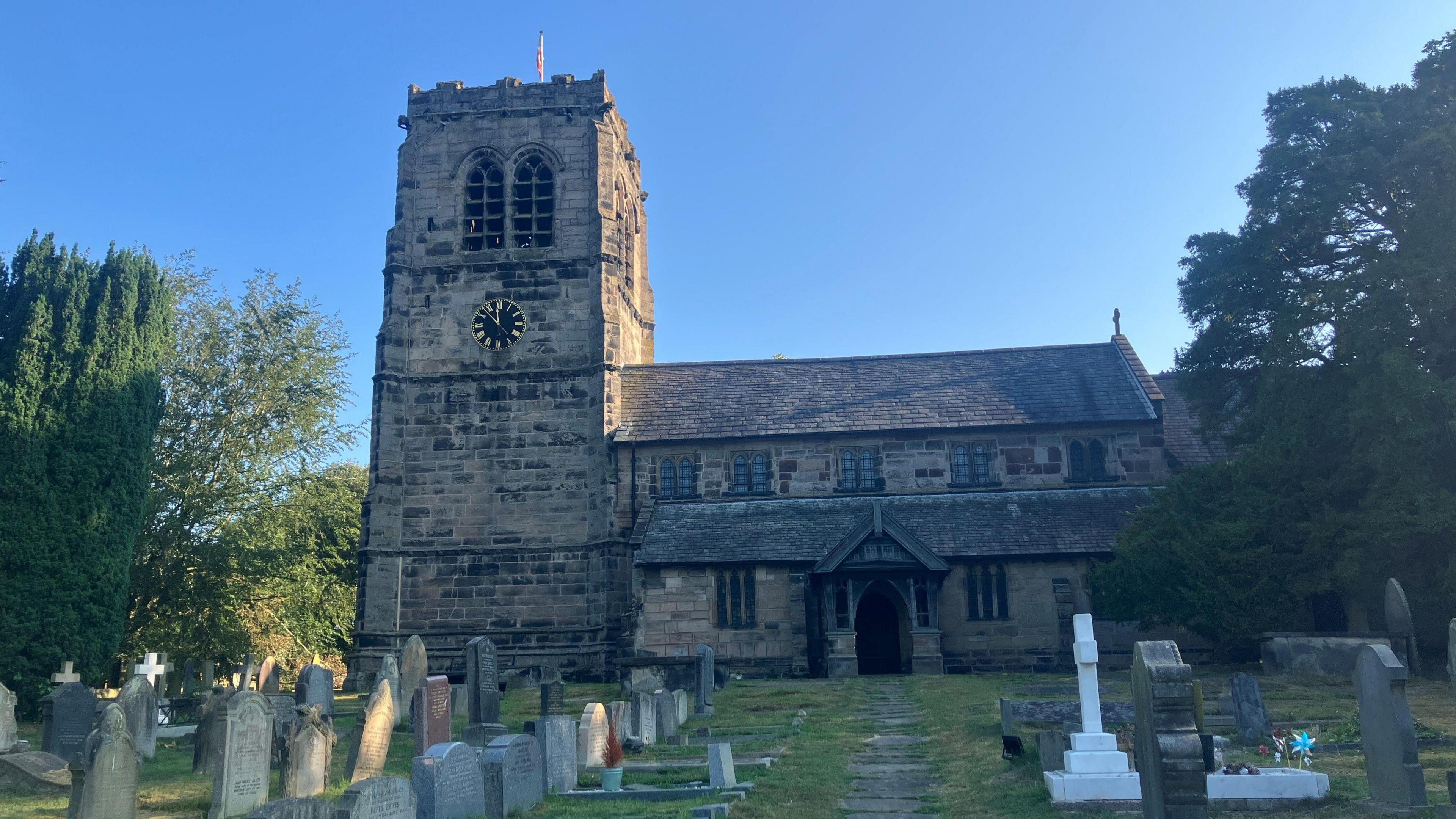 Photograph of St Wilfred's Church in Mobberley, Cheshire. The image shows a church and headstones in the graveyard.