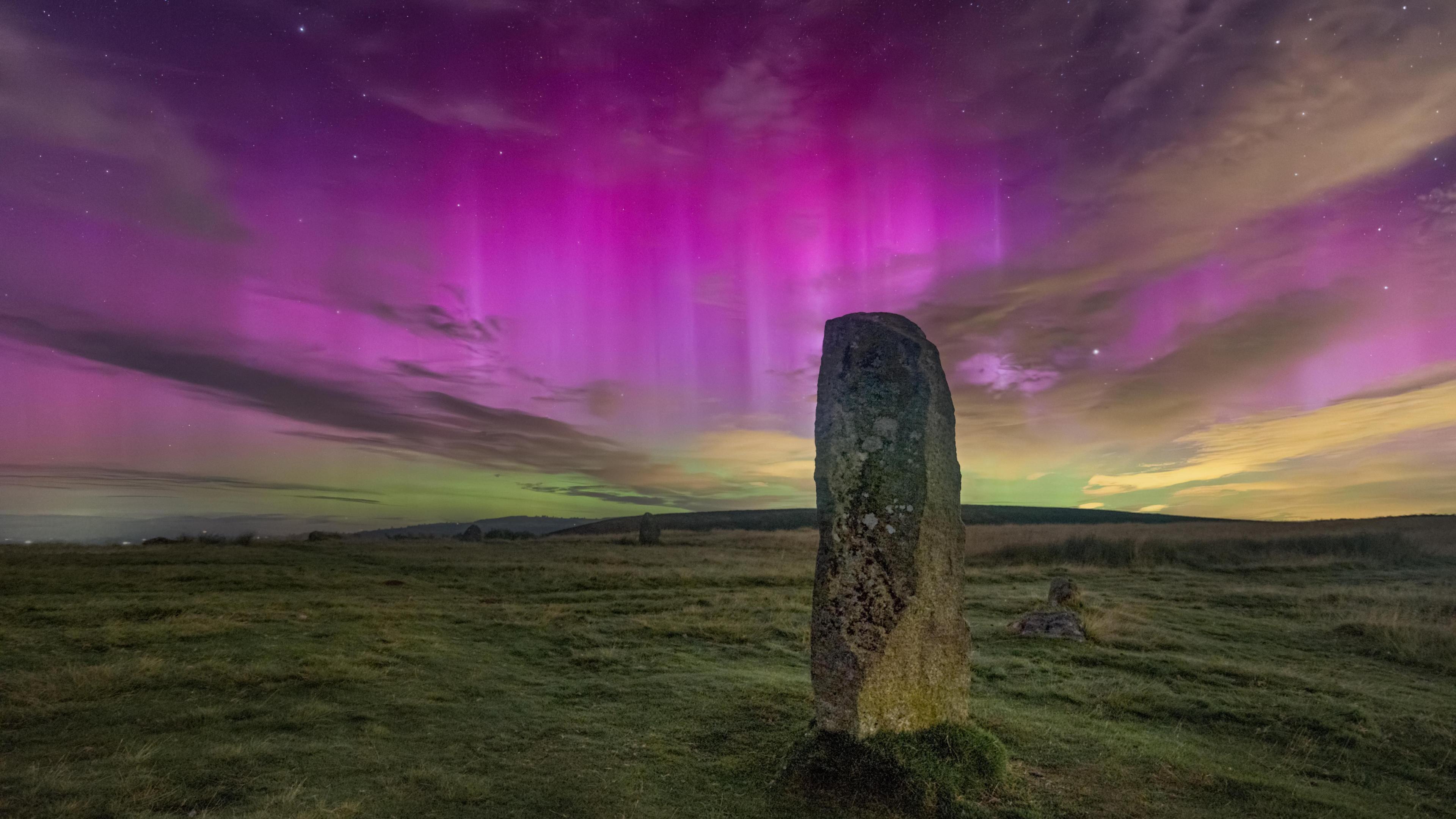 A standing stone with patches of lichen and a vivid purple sky behind it