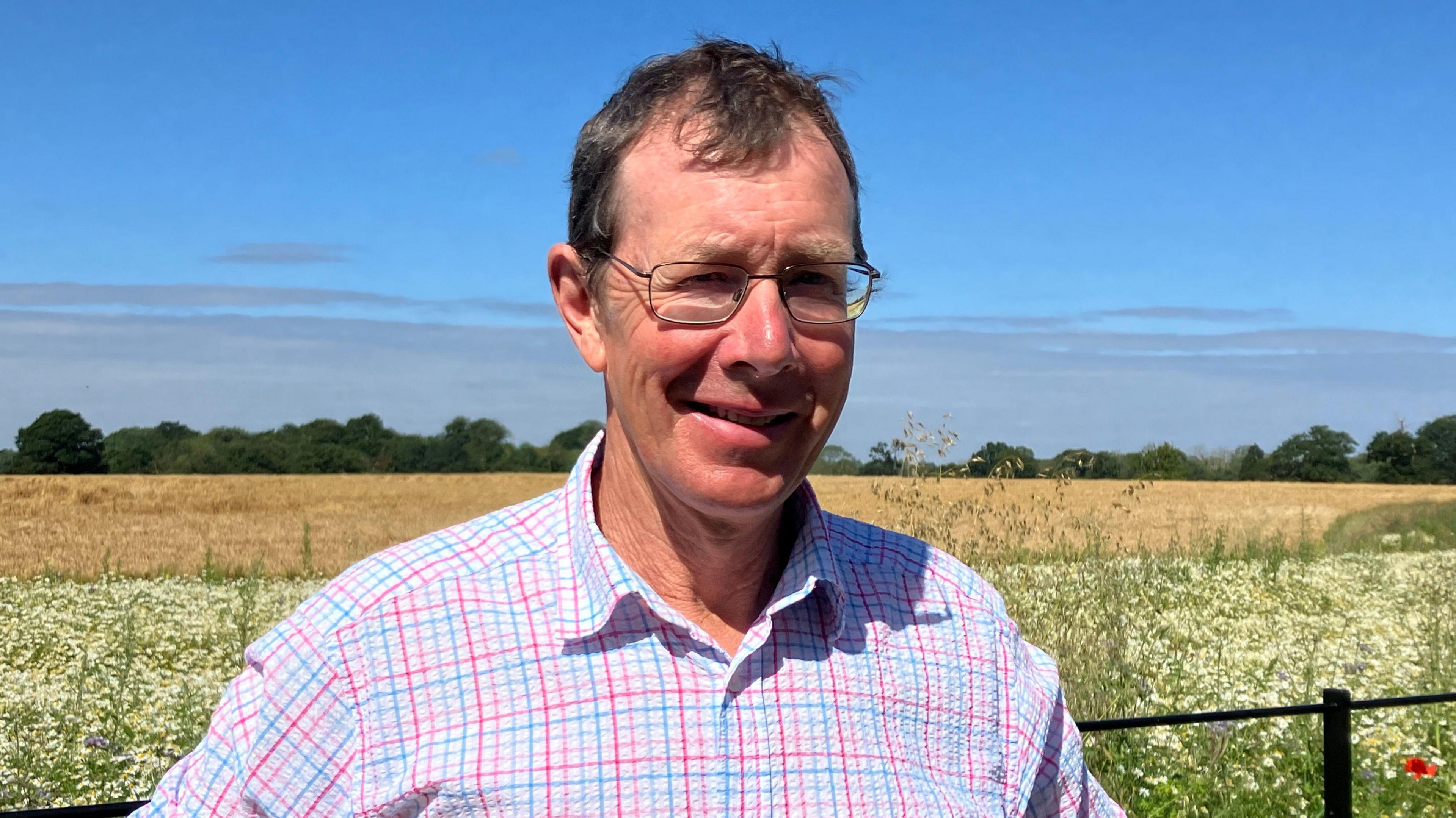 Farmer wearing a shirt and glasses stands in front of a field