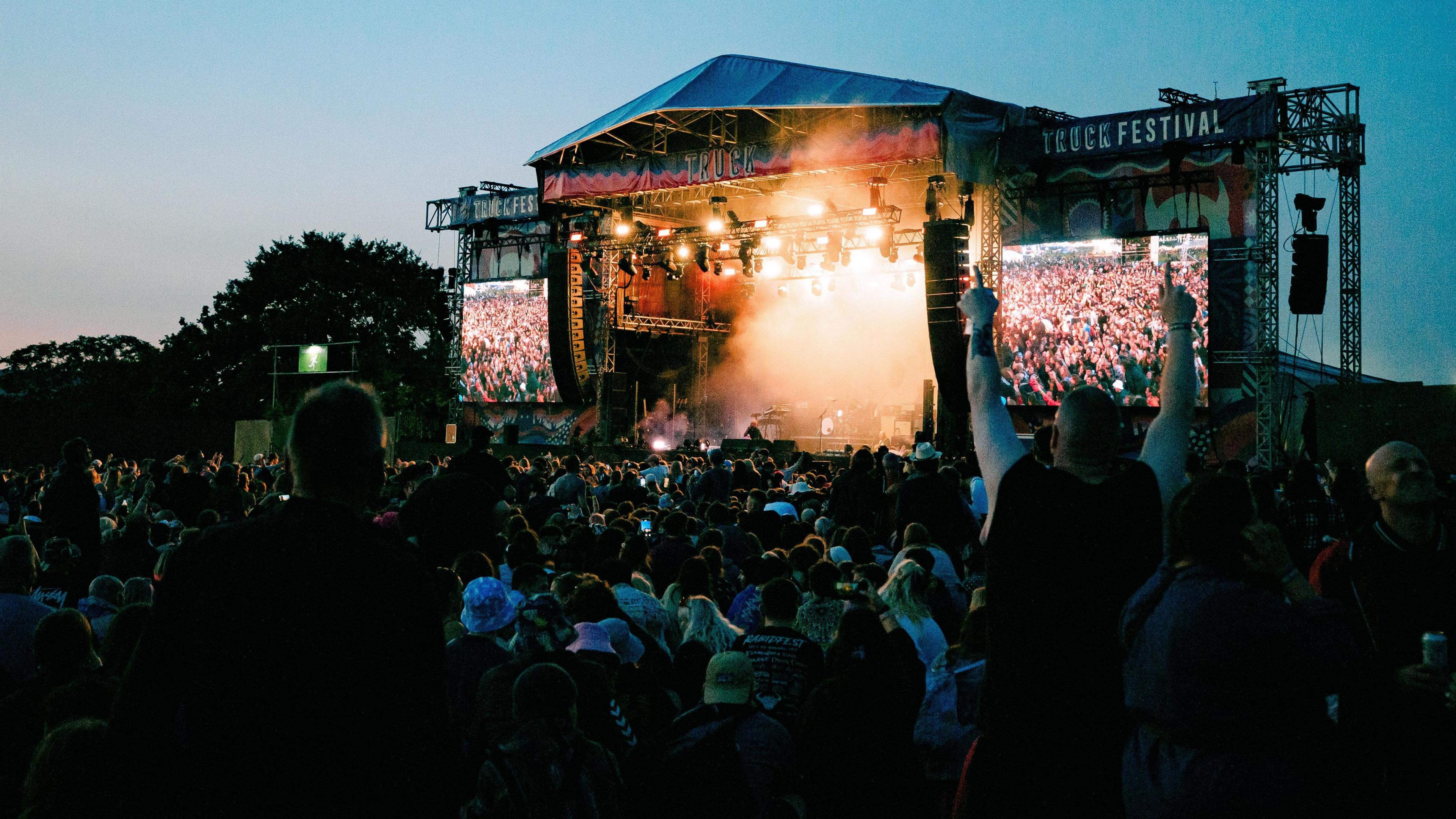 Crowds watch the main stage at Truck. Atmospheric smoke comes from the stage, and the crowds are pictured on the giant screens.