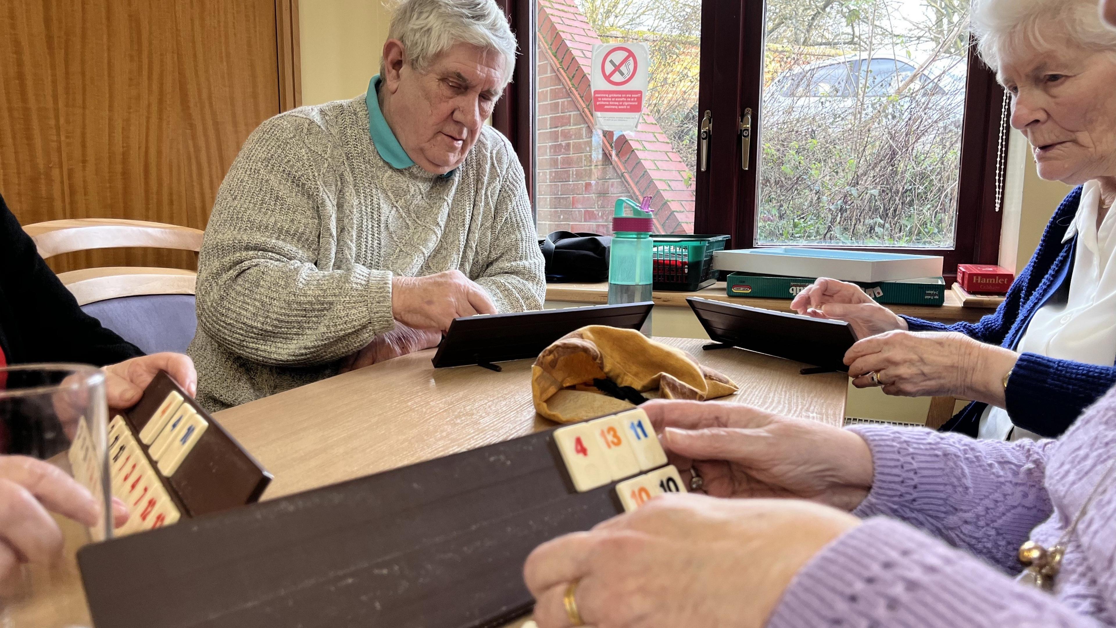 Older people sitting around a table playing a game with numbers on boards