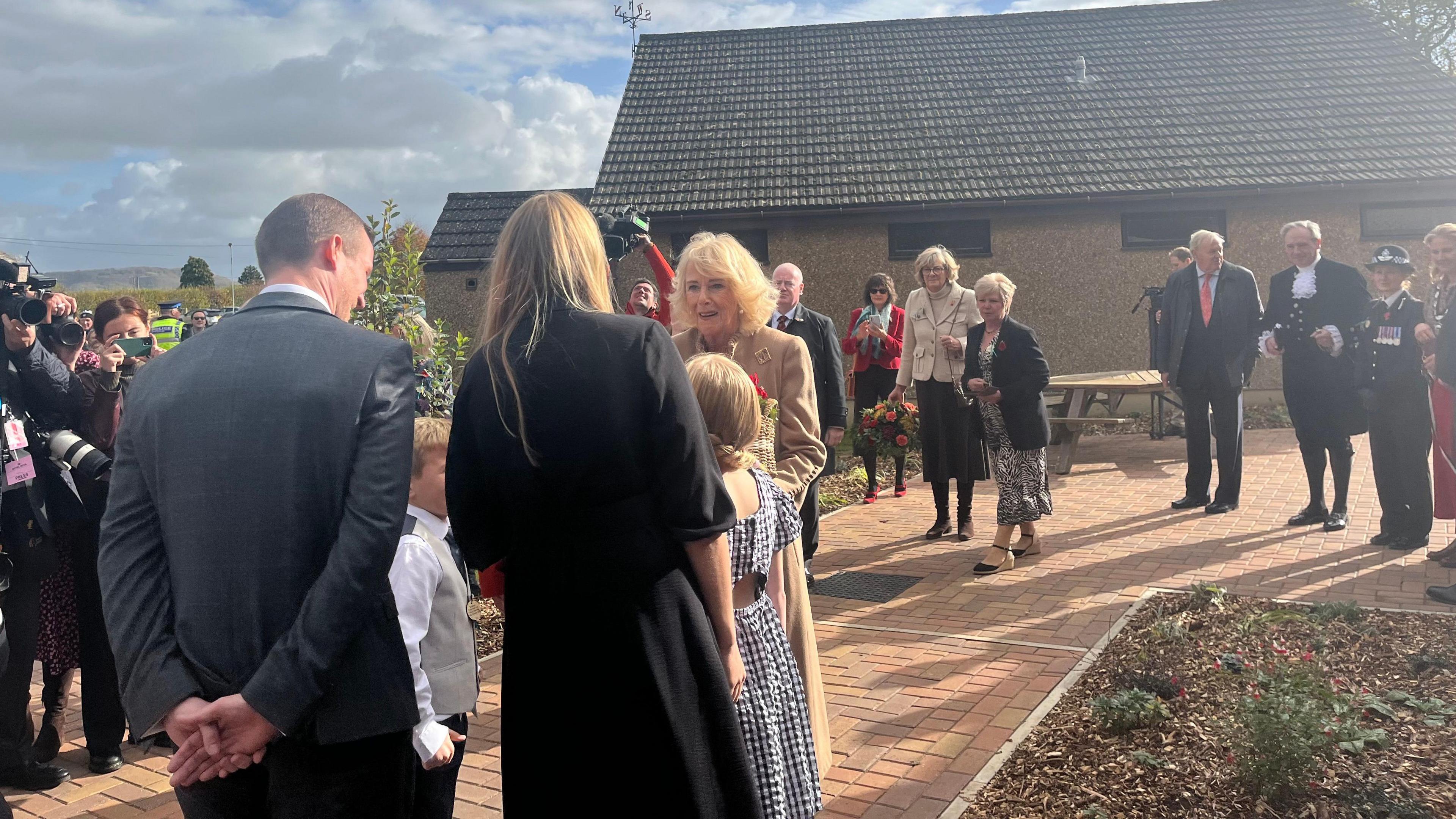 Camilla surrounded by people on a brick path with sun shining