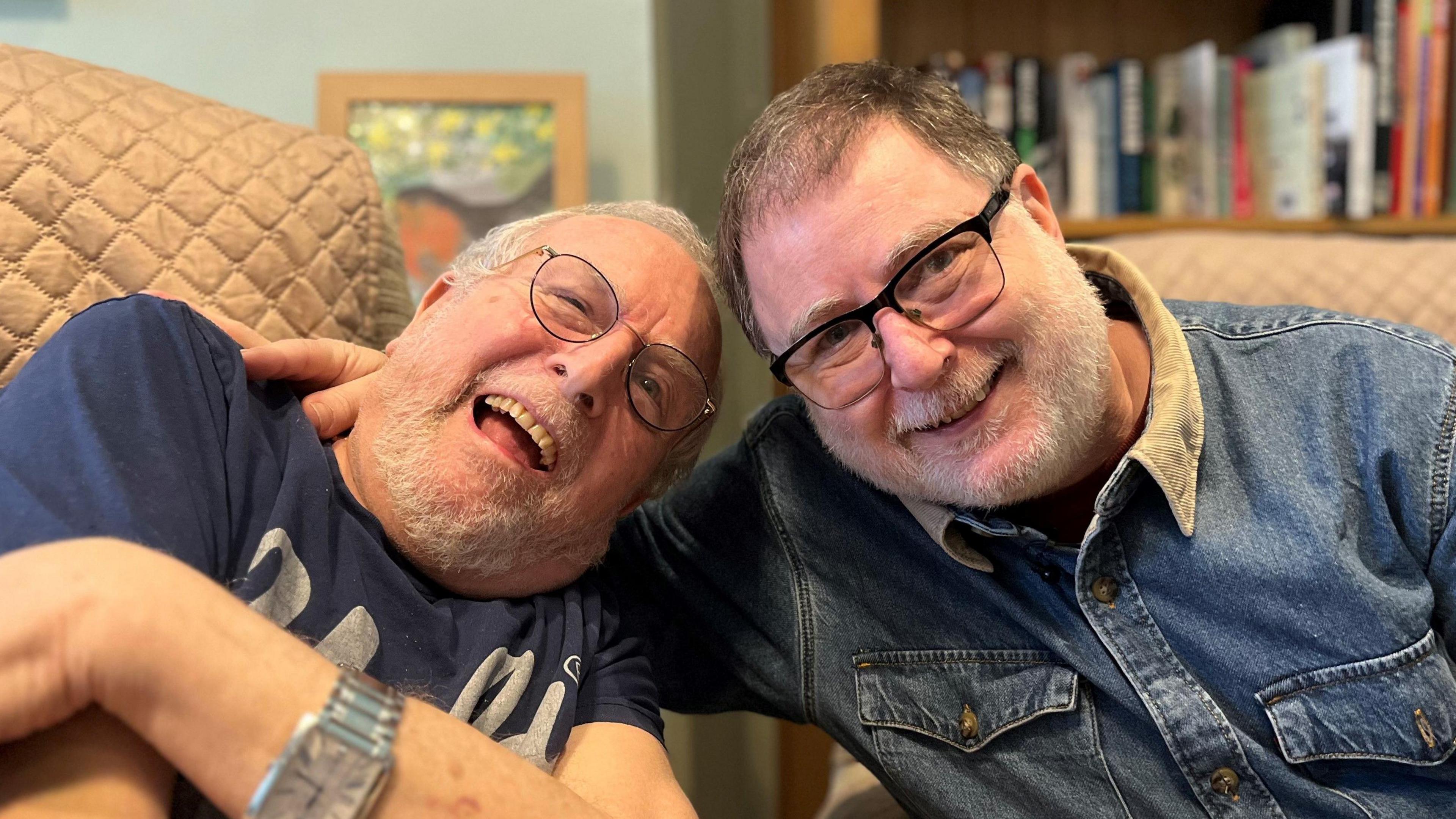 Bernard and Danny Mendoza, both smiling at the camera in a care home. Danny has his arm around his father.