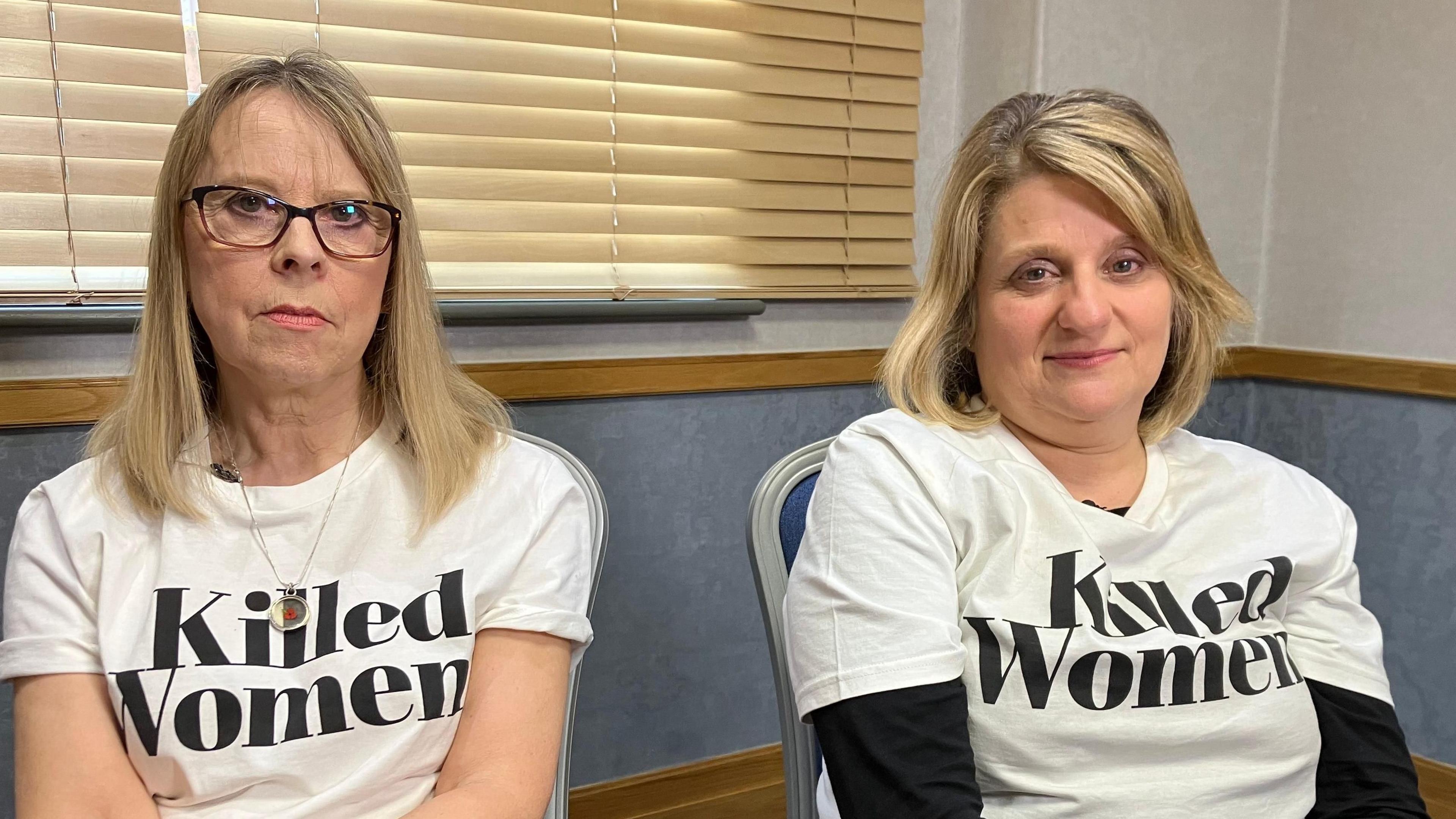 Julie Devey (L) and Carole Gould sitting on chairs, wearing white T-shirts with black writing, reading: "Killed Women", the campaign group they co-founded.