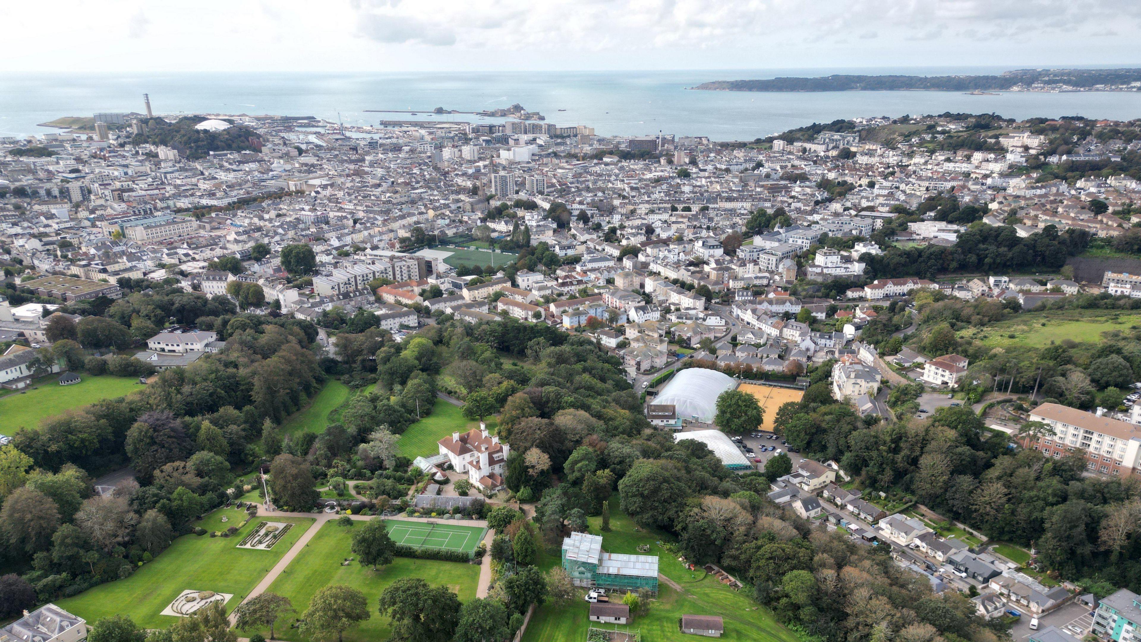 A view of St Helier from above. Trees, rooftops and the coast is visible  