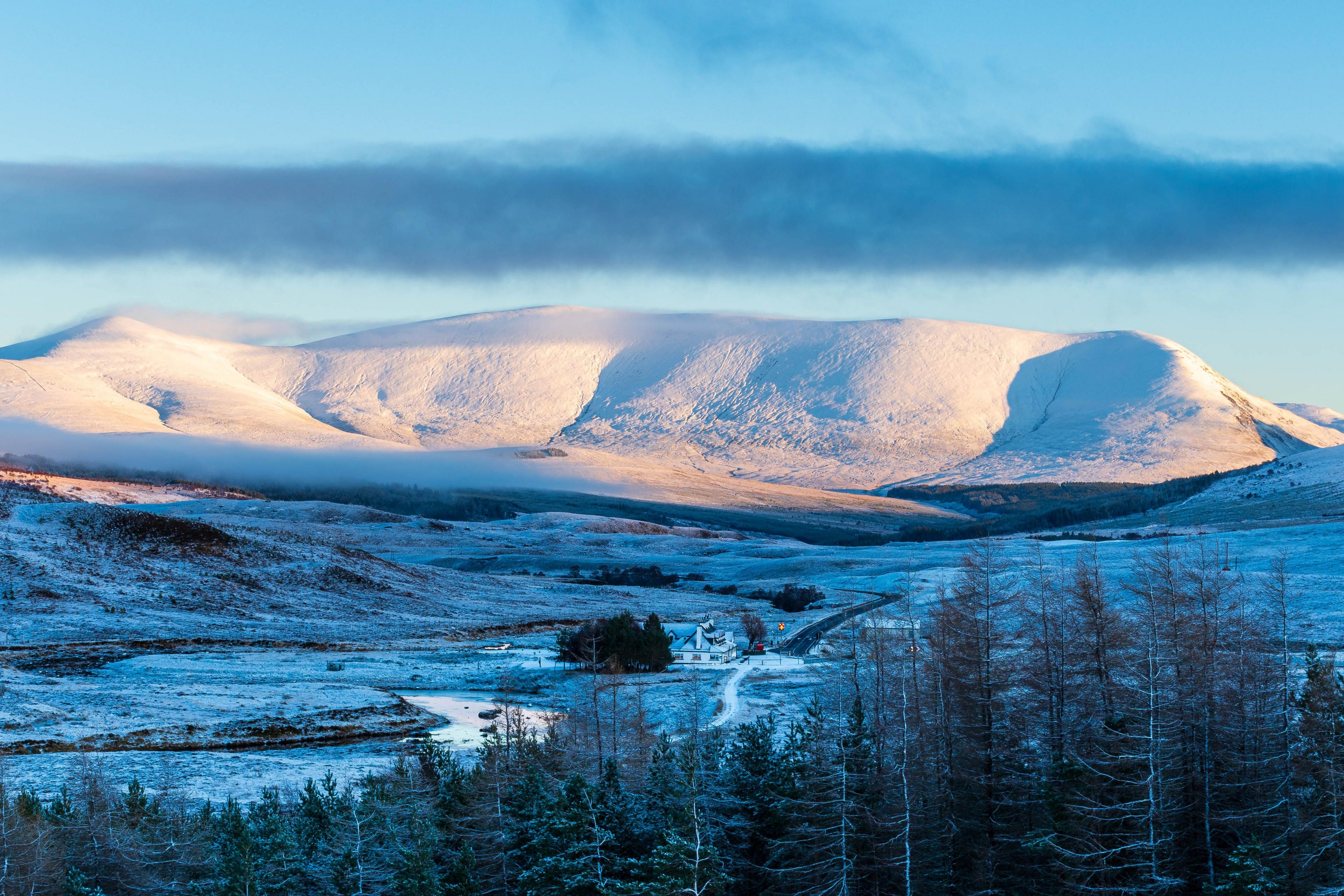 A distant mountain covered with snow and a valley below which is also dusted with white with trees in the foreground