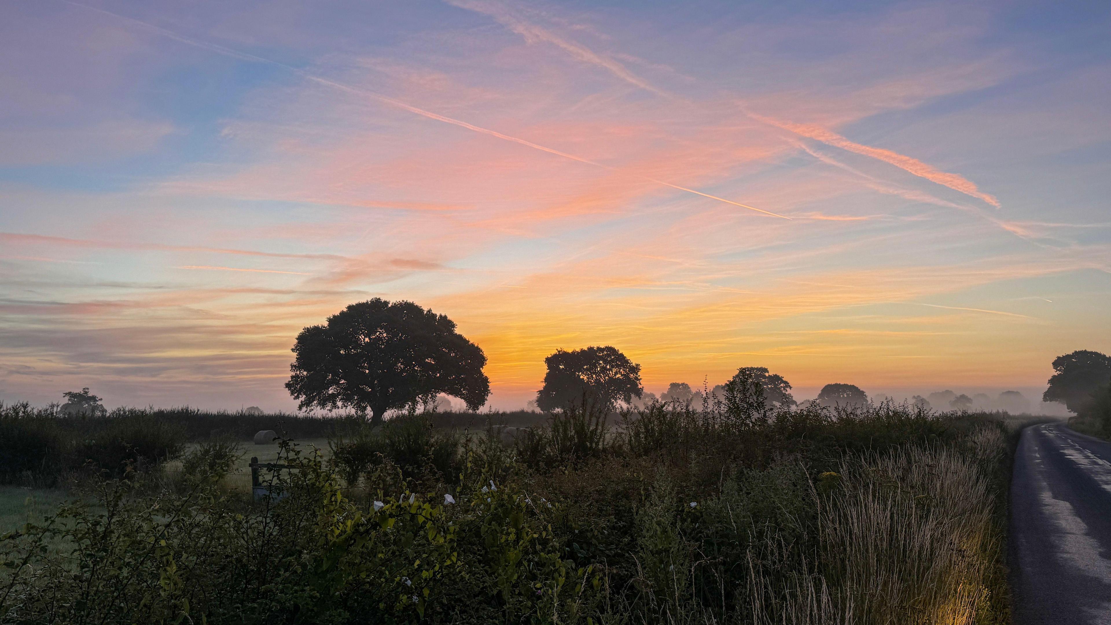 Morning mist across a farmers' field at dawn with an orange glow lighting clouds in the sky