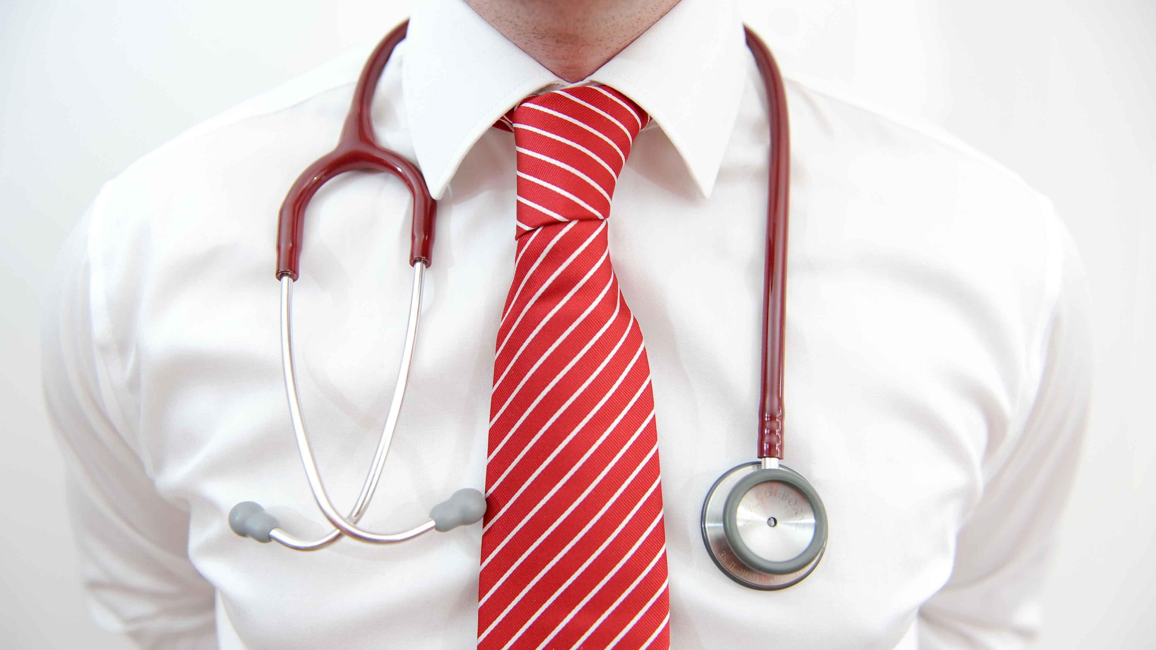 The chest of a doctor wearing a white shirt with a red striped tie and a stethoscope around his neck.