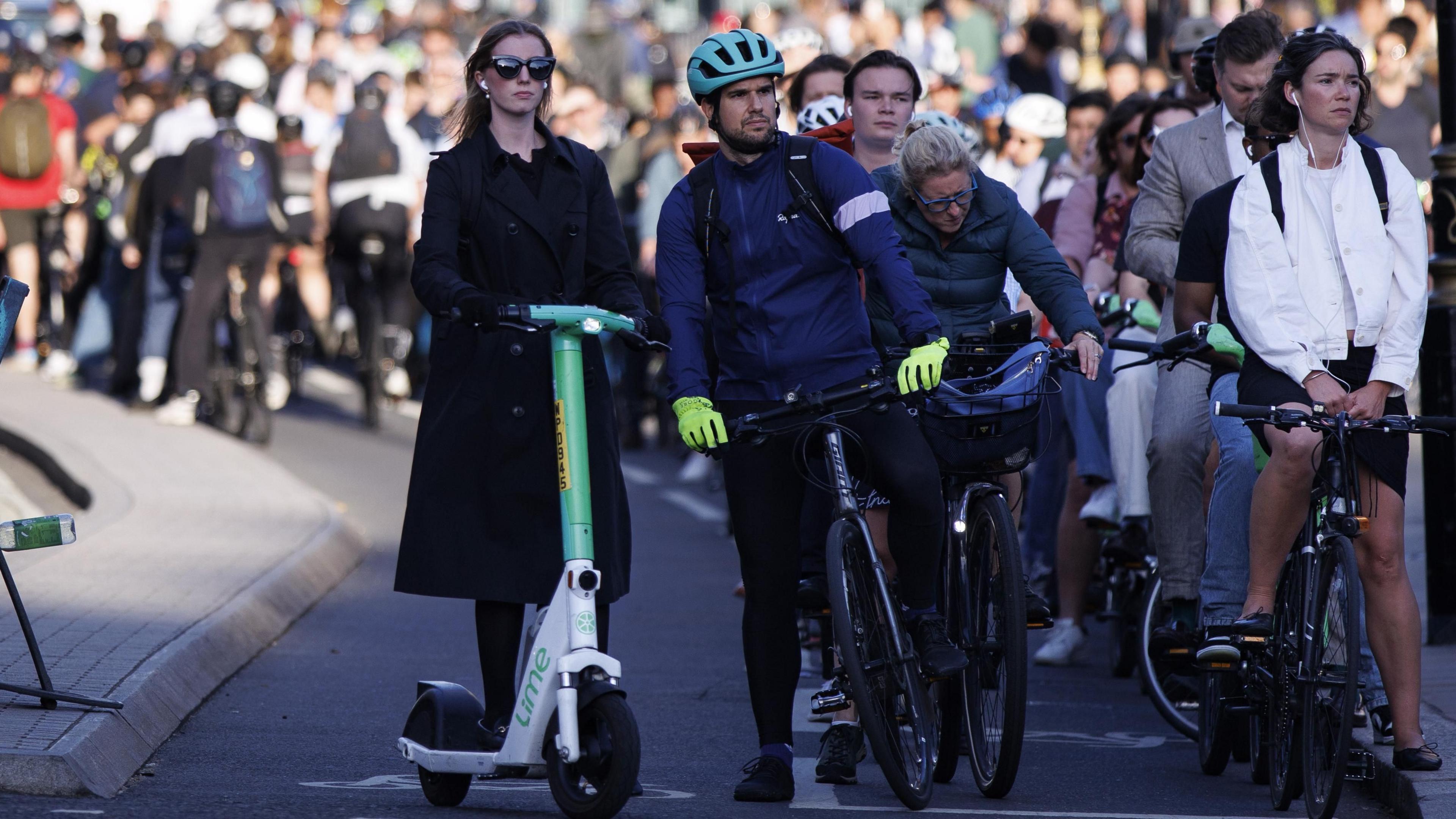 A woman is standing on an e-scooter next to cyclists