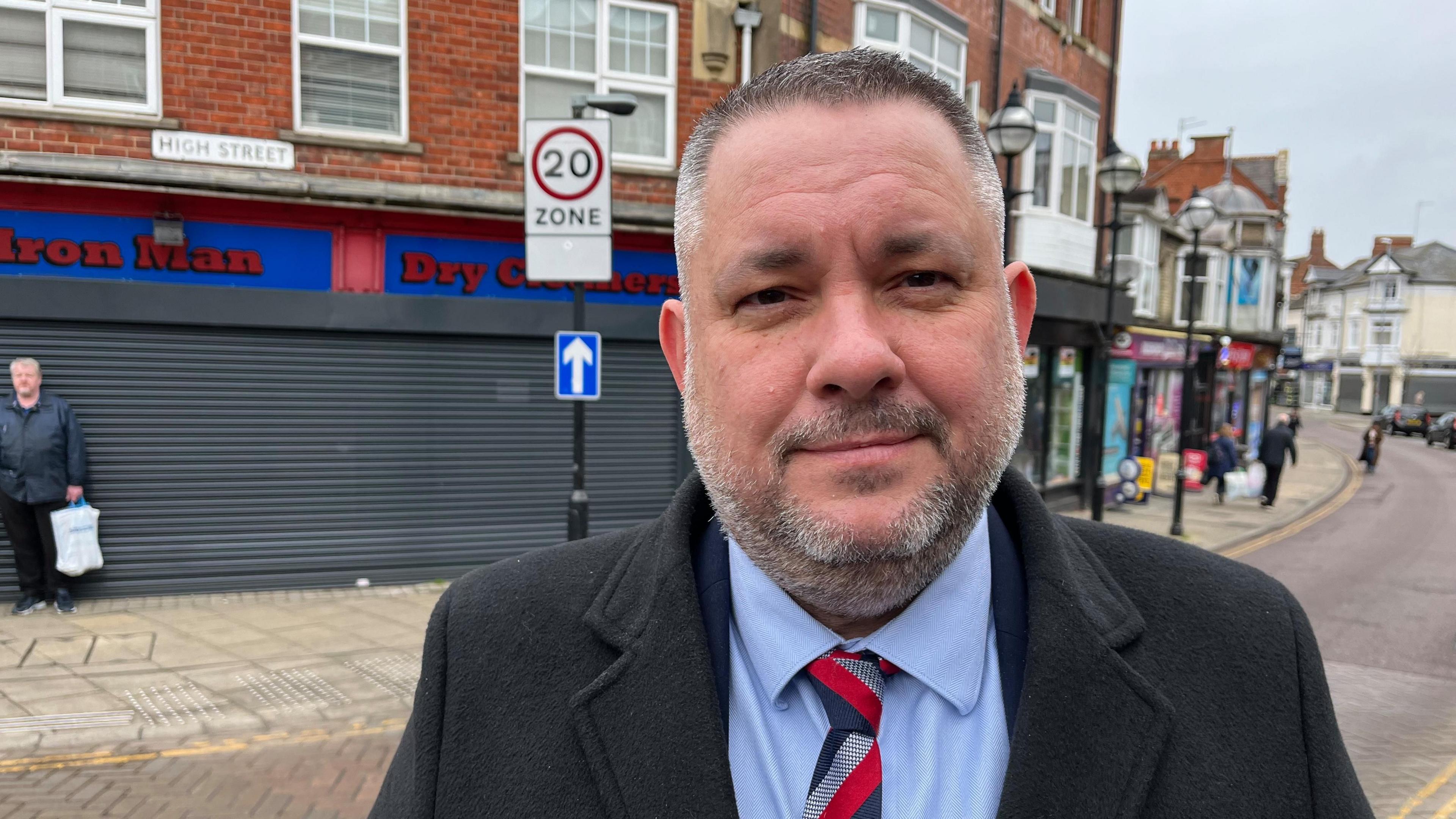 Jason Smithers standing in the street with a striped tie and a black coat