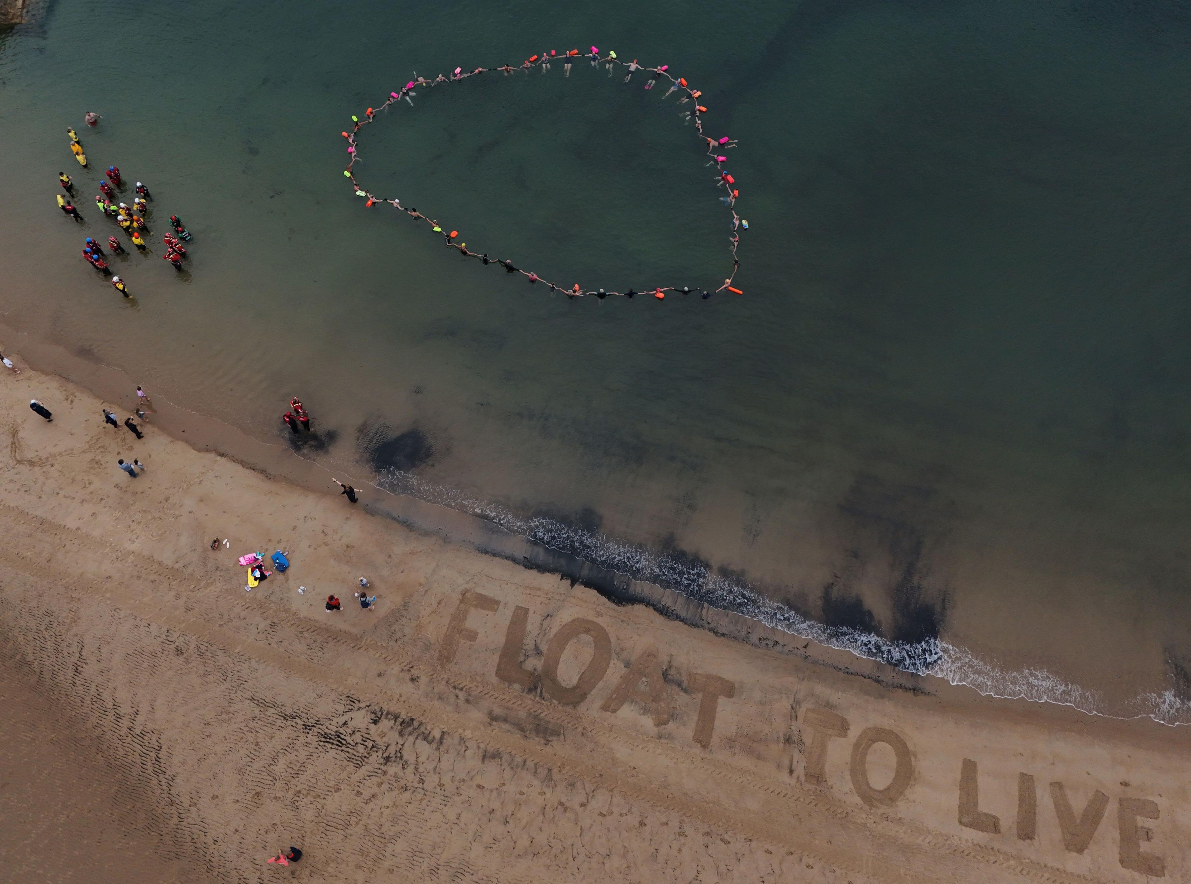 aerial image of a beach. a group of people are floating in the sea and the words "float to live" and drawn into the sand