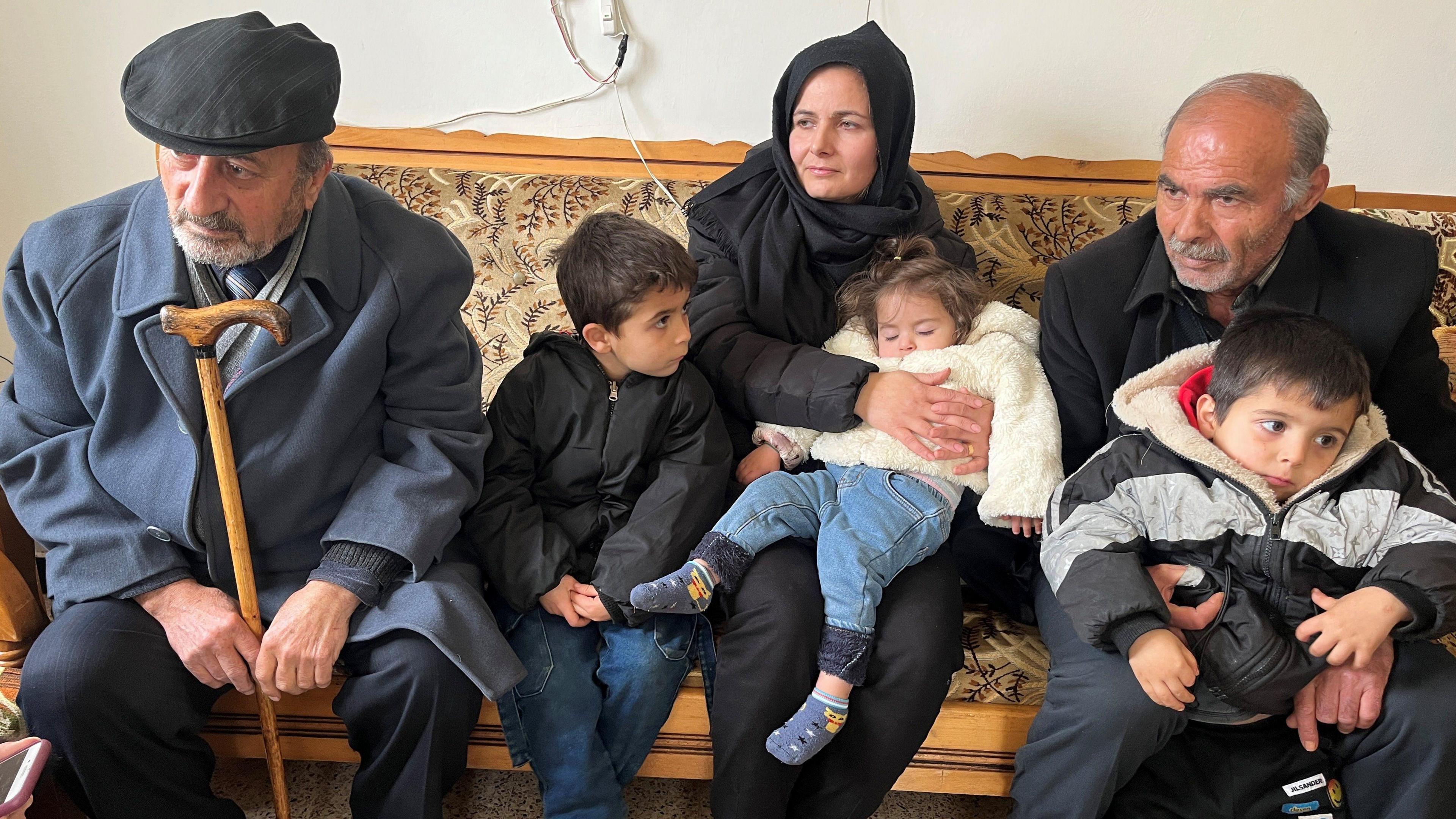 A woman, three young children and two older men are seen sitting on a bench.