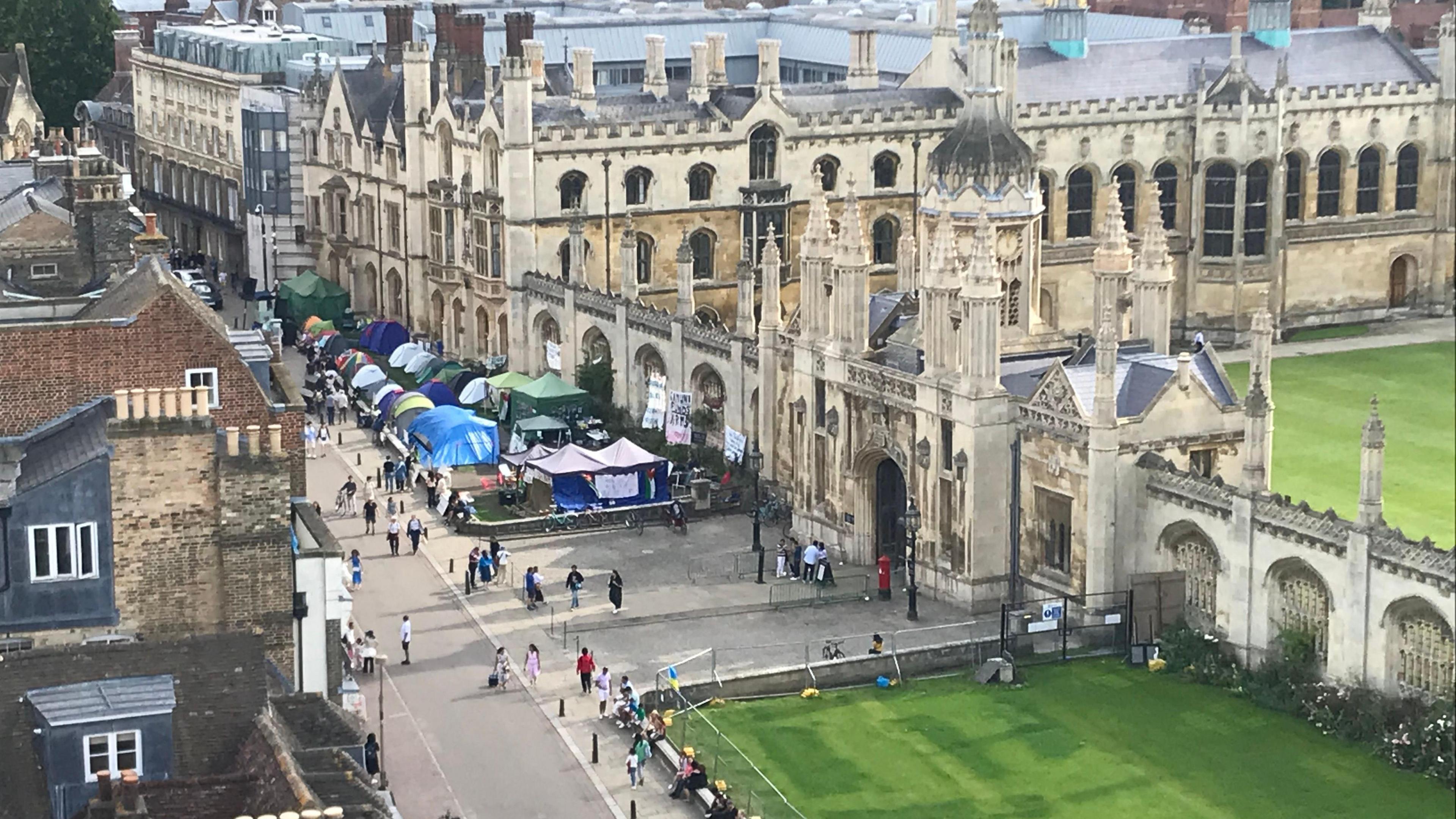 High shot taken at Great St Mary's Church of the Gaza protest camp in Cambridge, showing a collection of tents and placards on the green space in front of a College