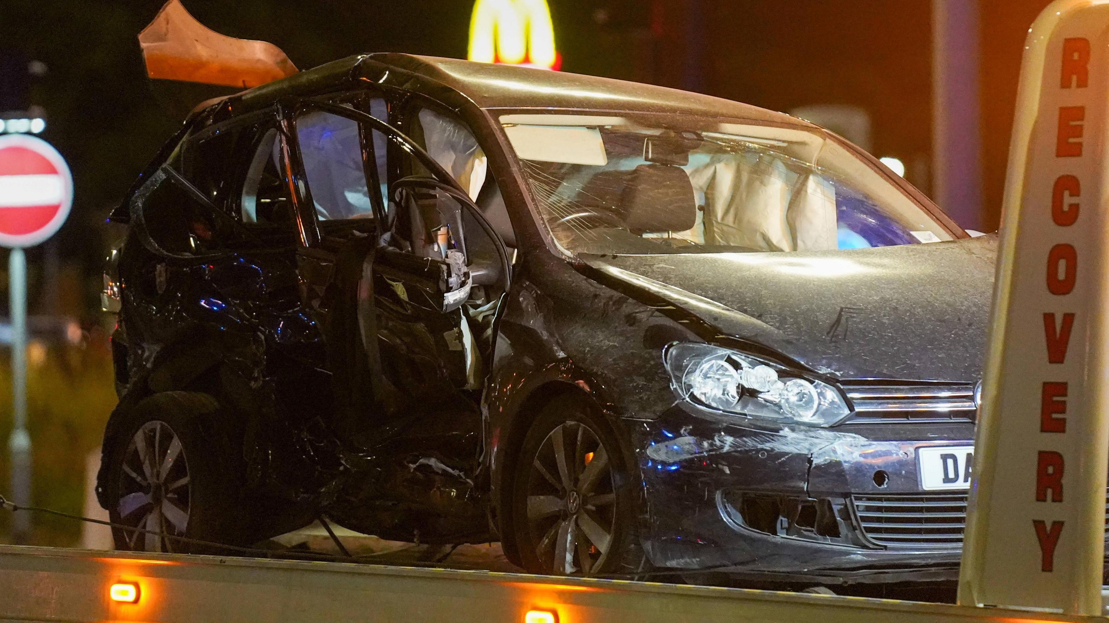 A badly damaged car which has been caved in on the drivers side. The airbags have been deployed.