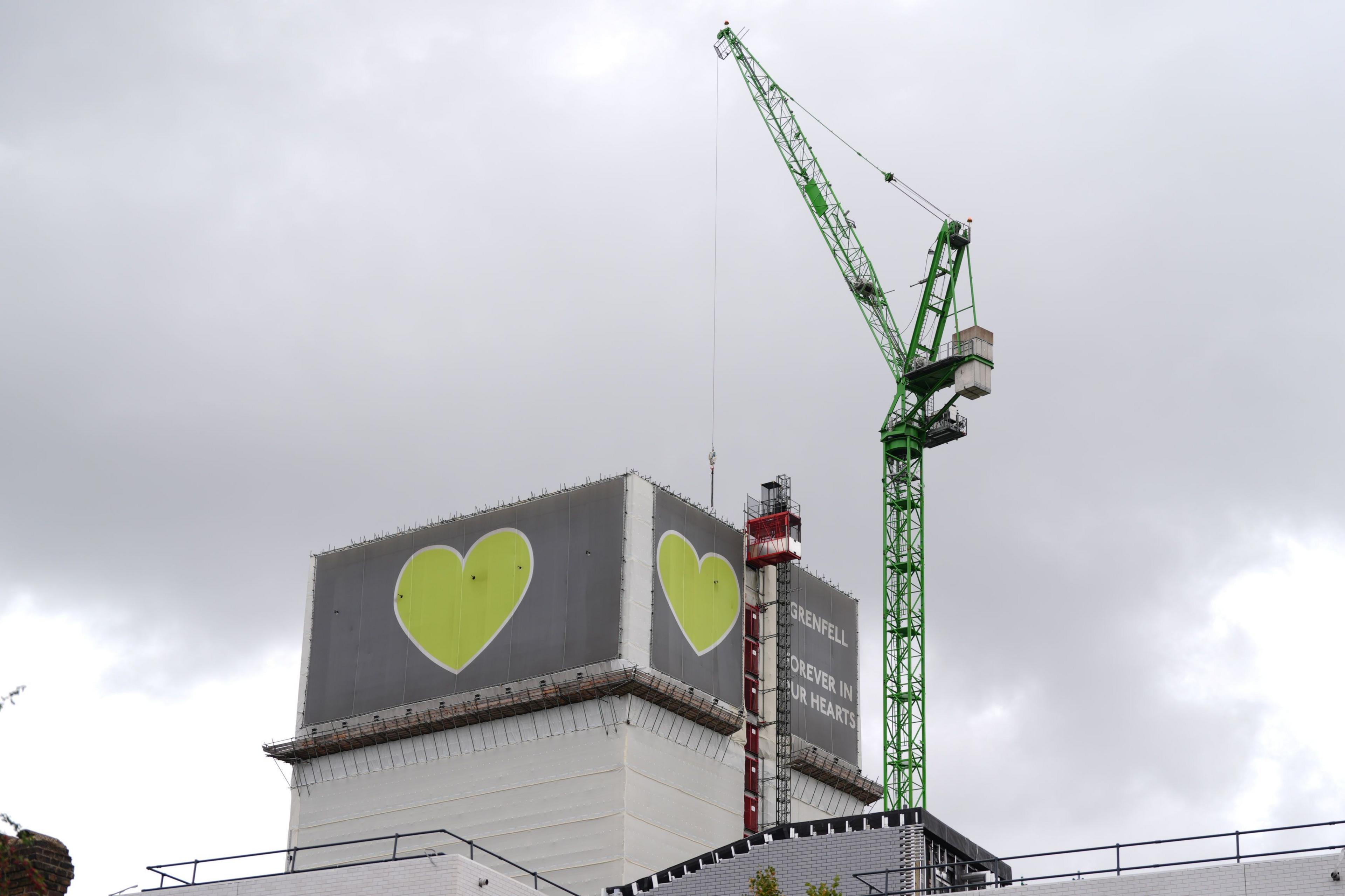 A crane is seen over the Grenfell Tower in west London where a large green heart is still visible on the top floors of the tower block