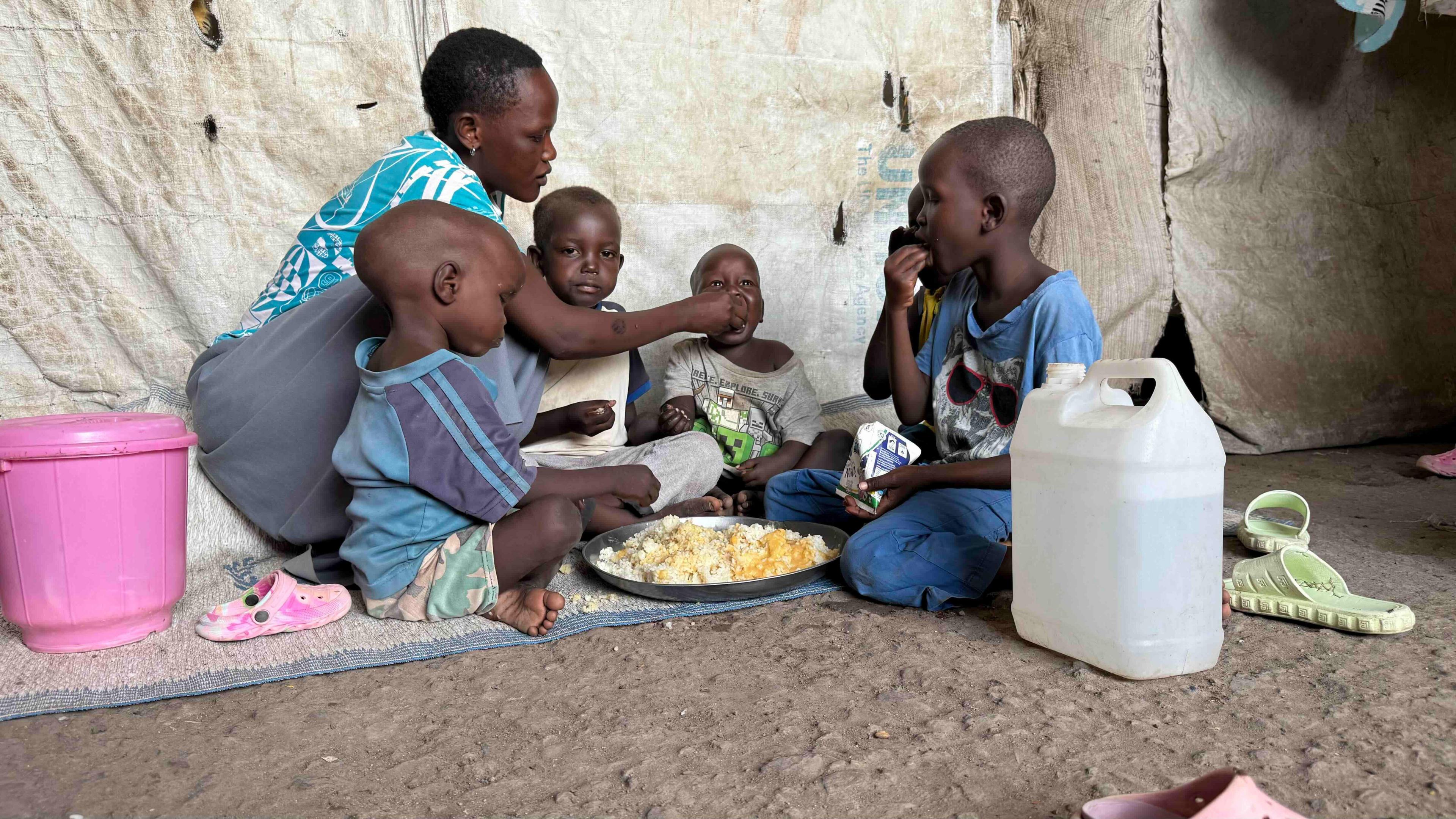 Sitting on the ground, Agnes Livio feeds her children from a large silver plate