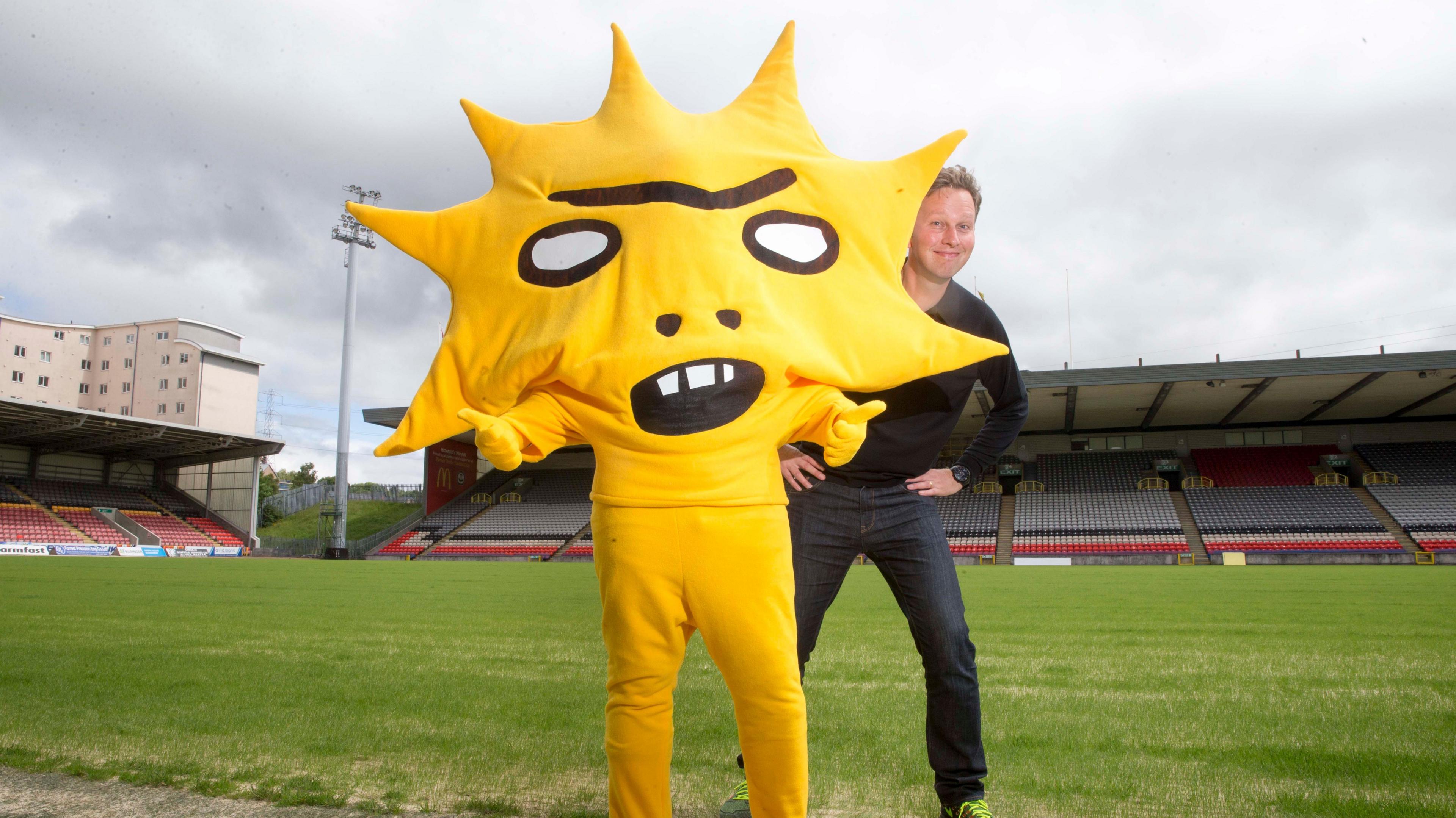 Artist David Shrigley with a mascot that looks like a yellow star with a face on it