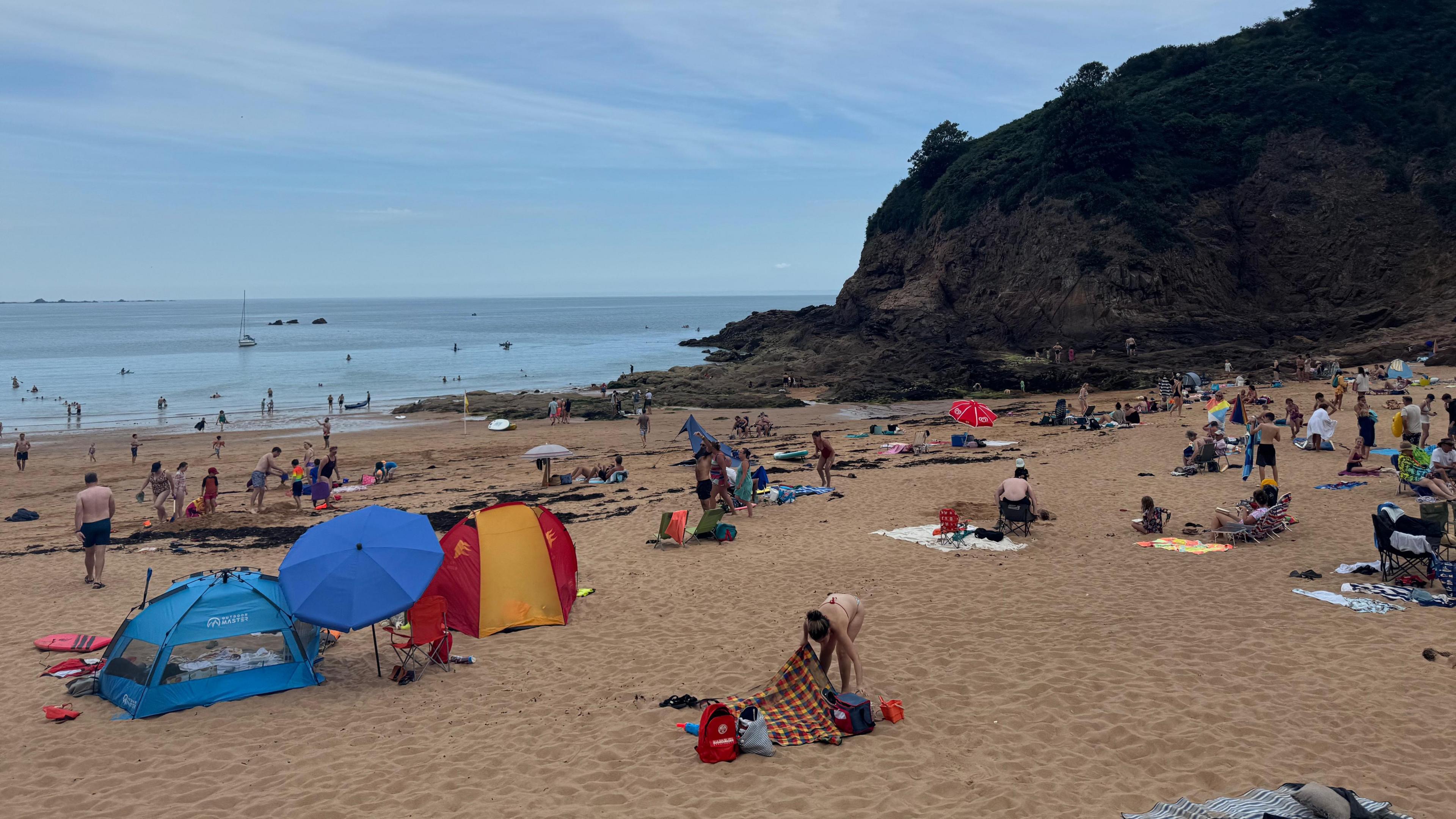 Dozens of people at the beach with the sea on the left and cliffs on the right.