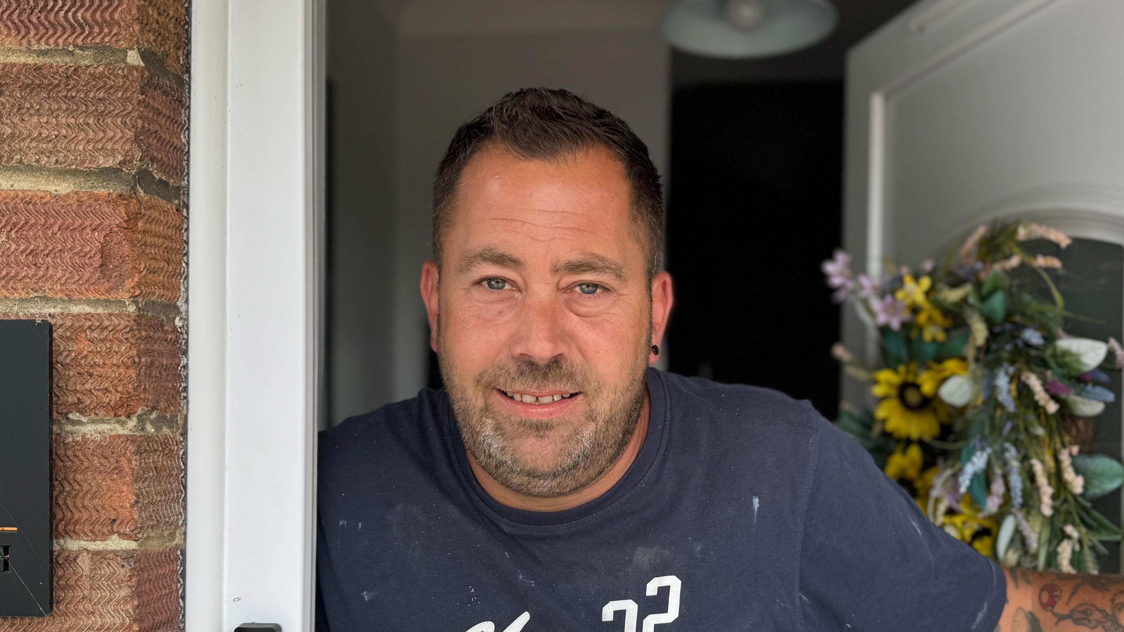 A head and shoulders image of Shaun Farrell. He is wearing a navy t-shirt and standing in his doorway. He is looking into the camera.