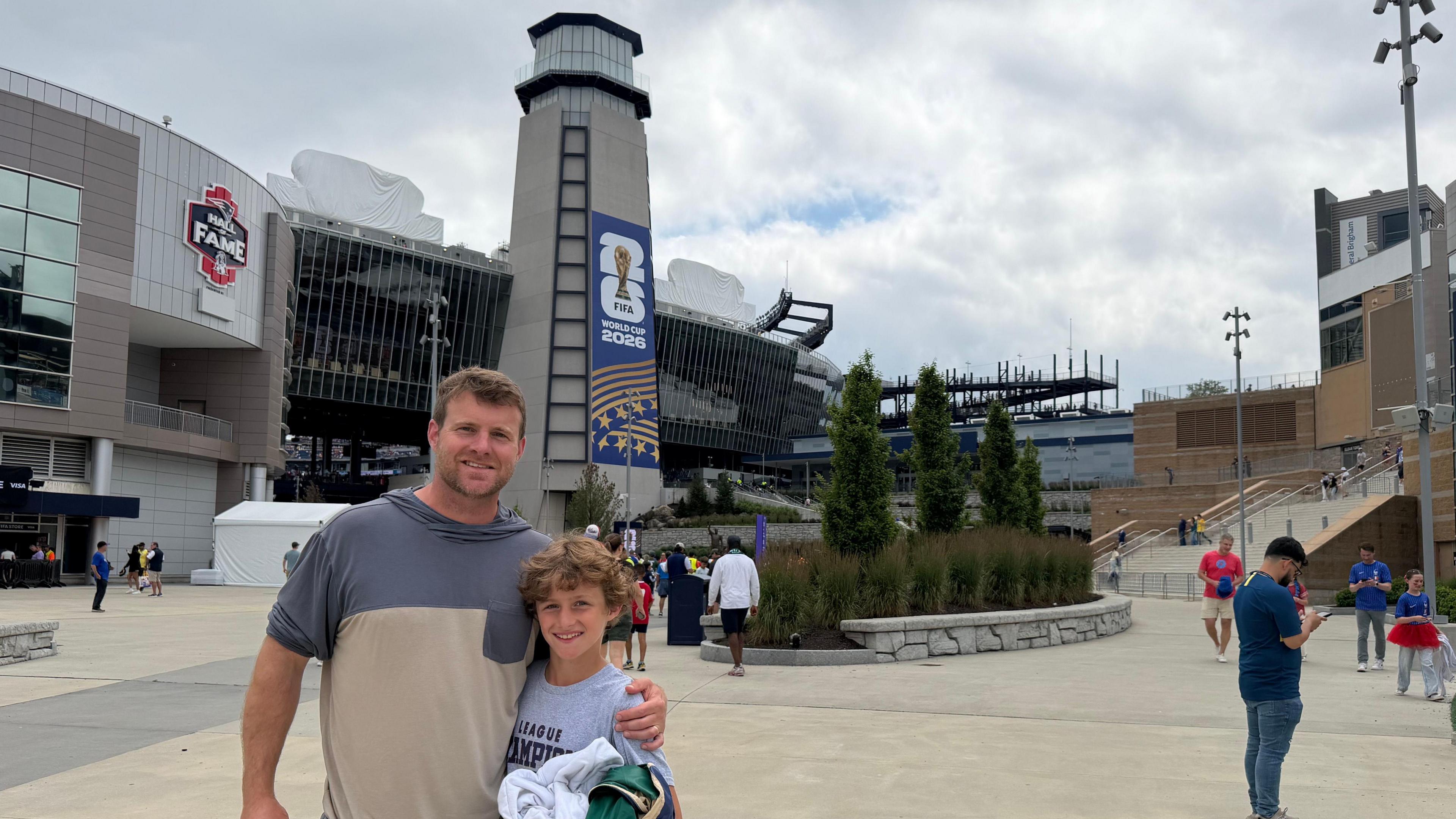 Eben Pingree holds a black hoodie in his right hand as he stands with his left arm around his son Cole in front of the Boston Stadium