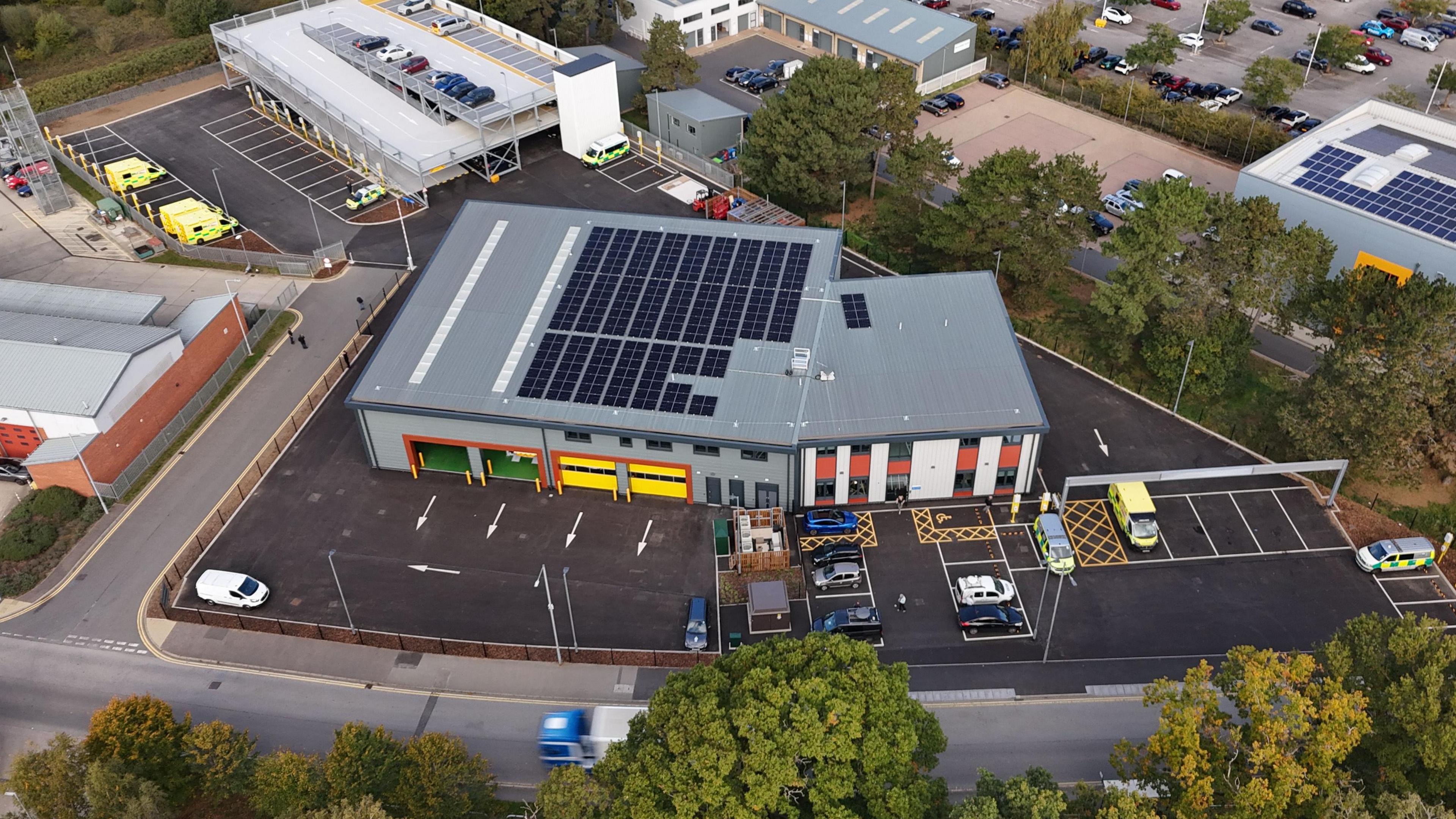 An aerial photograph of a new ambulance hub which has a grey multi-storey in the left corner and the main building in the centre. Both structures have parking bays outside.