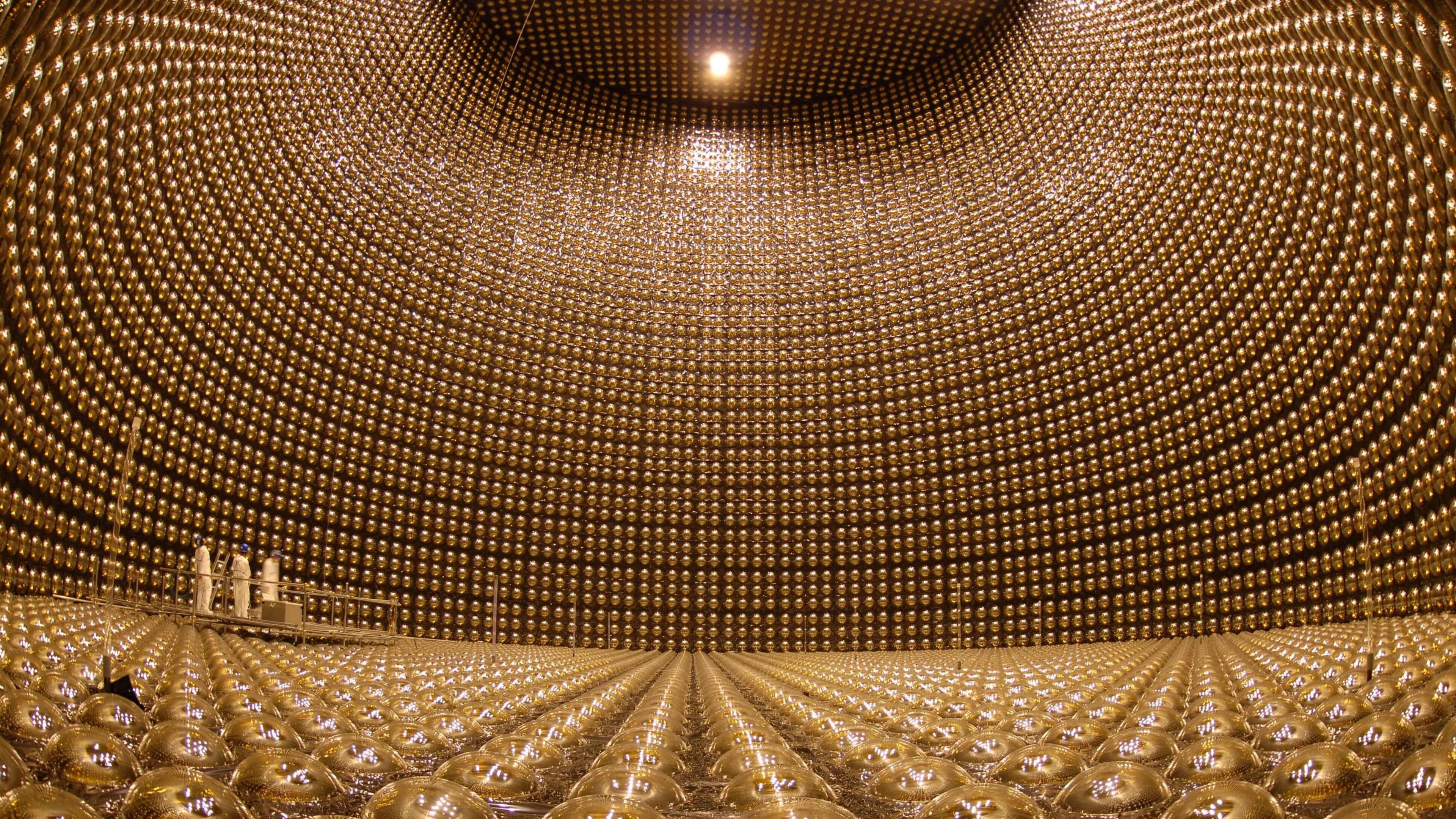 A giant room filled with gold colouted globes forming the floor and the curved walls. In the background three scientists can be made out dwarfed by the scale of the complex