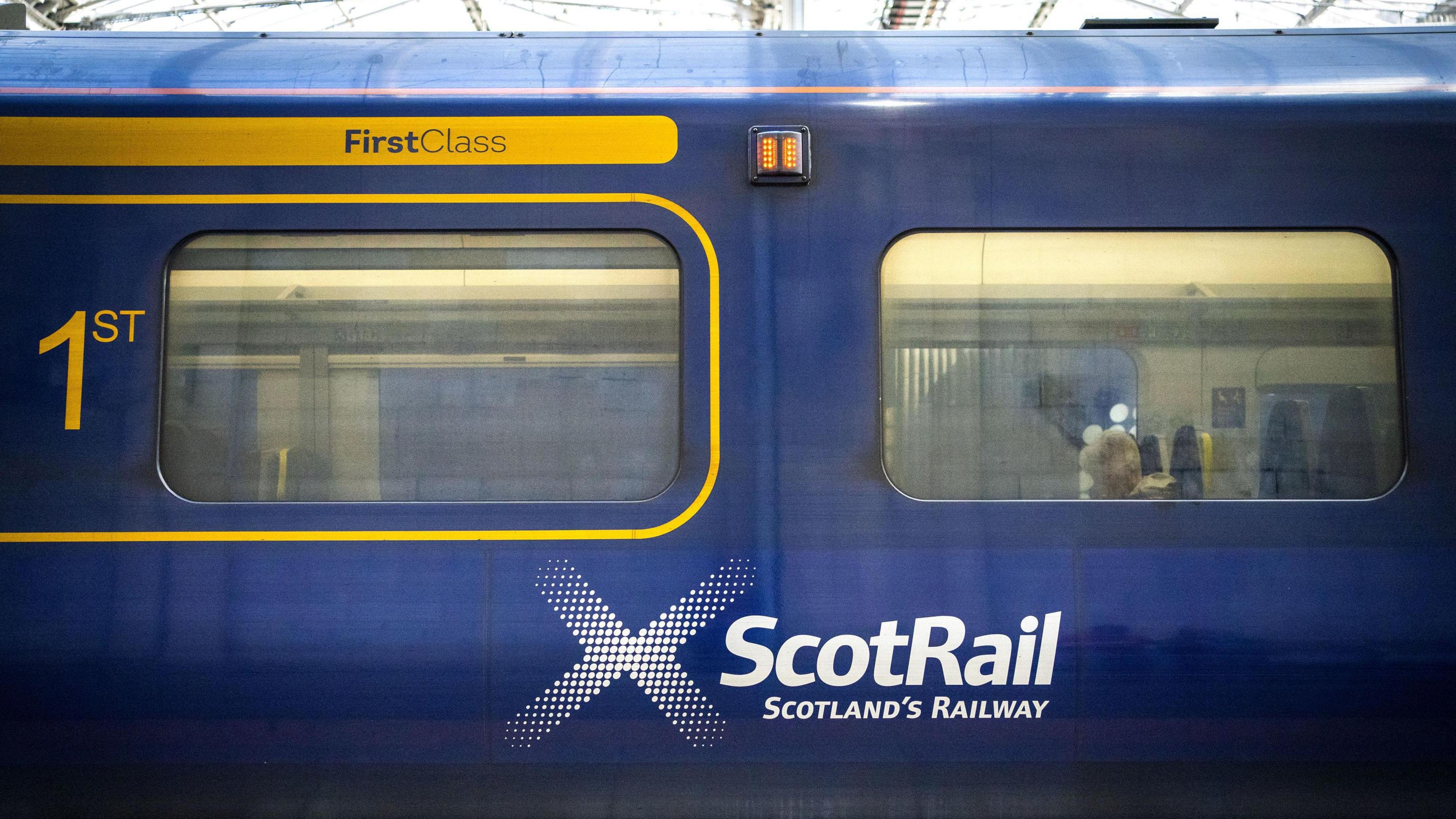 A tight shot of a ScotRail branded train with a grey-haired woman just visible through the dirty window.