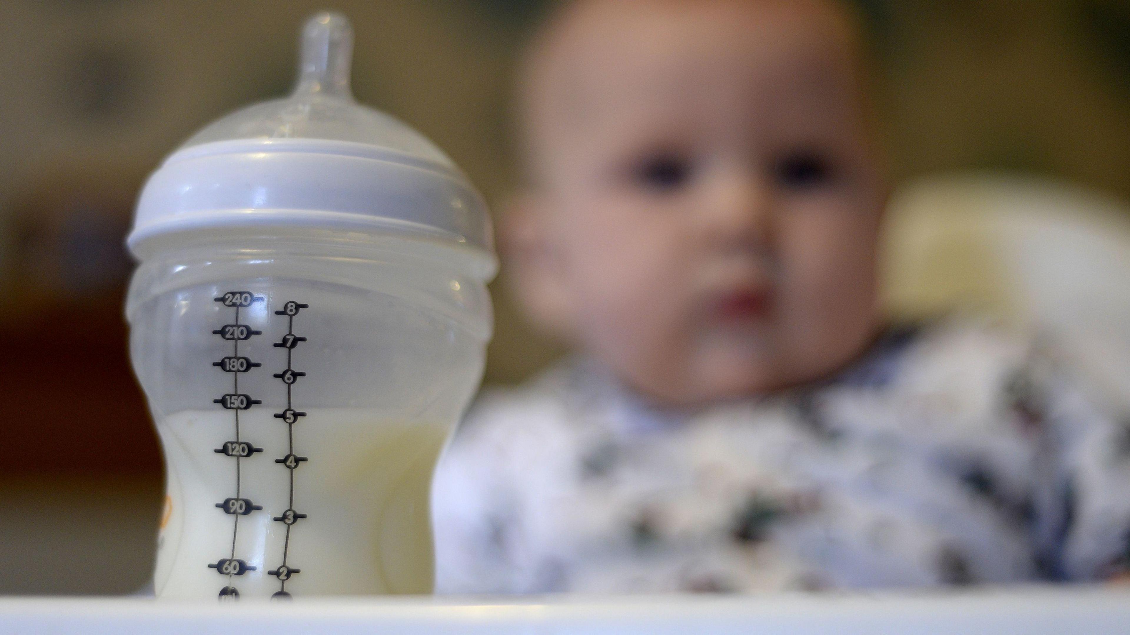 A feeding bottle of milk with a baby in the background