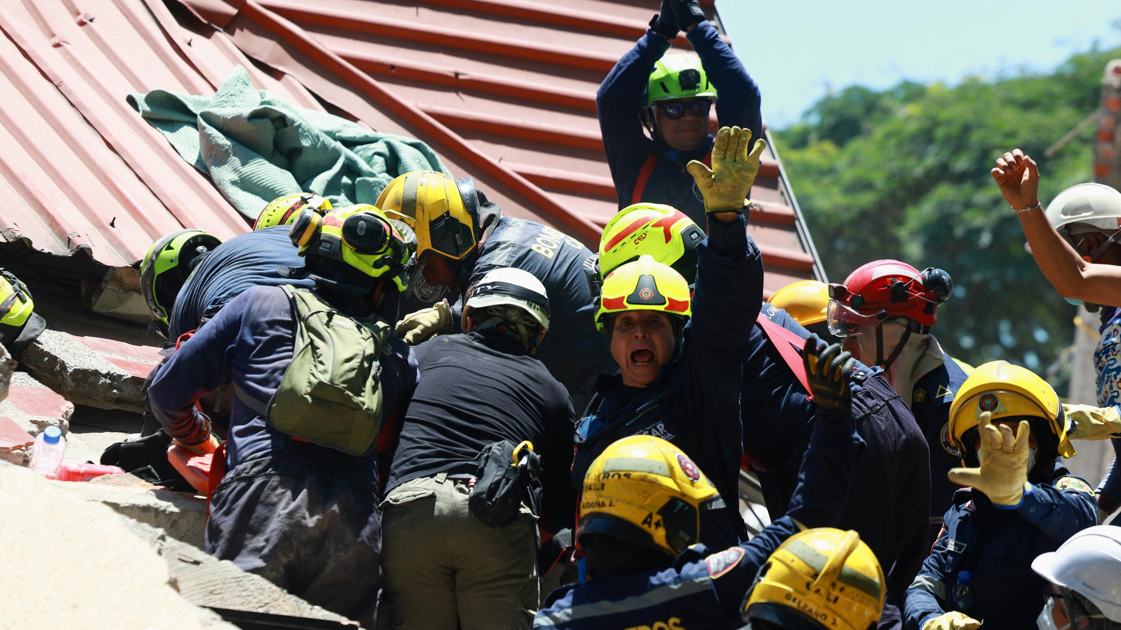 Firefighters react as they rescue a person following an earthquake, in Cali, Colombia, August 11, 2026 - one can be seen prominently in the middle, holding his arm up and appearing to shout 