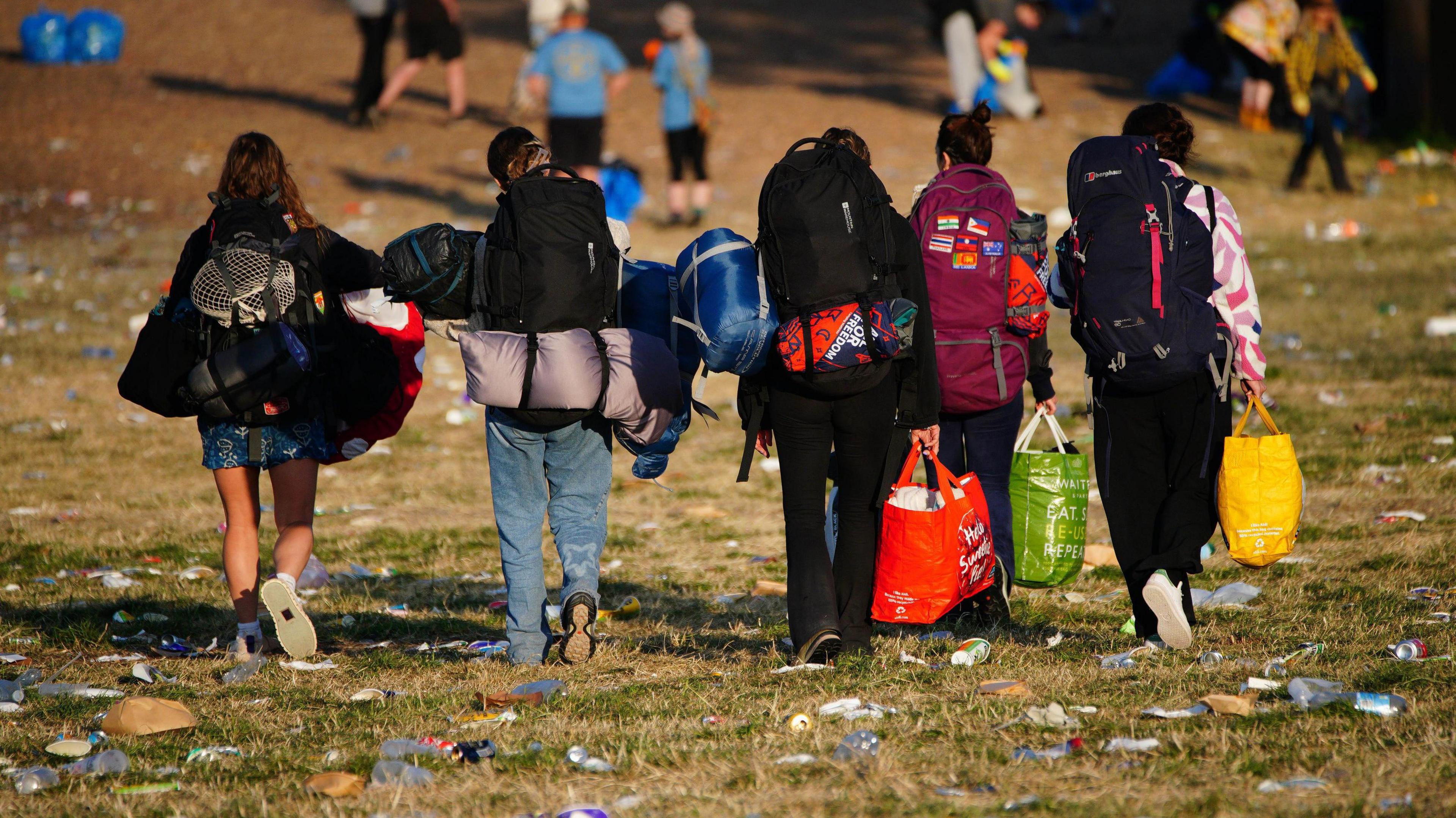 People walking with rubbish and bags in a green field