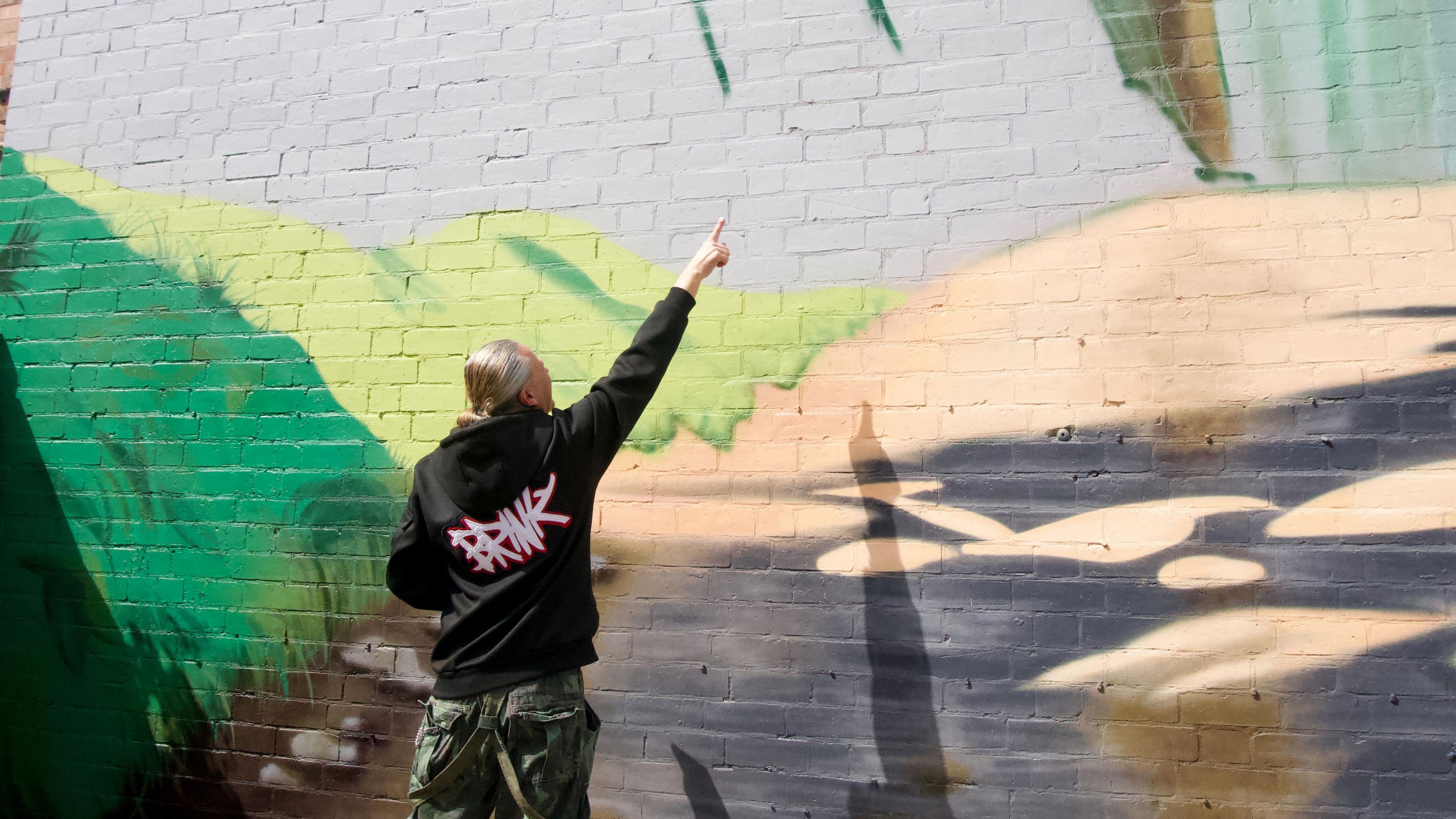 Man next to mural being painted on side of house