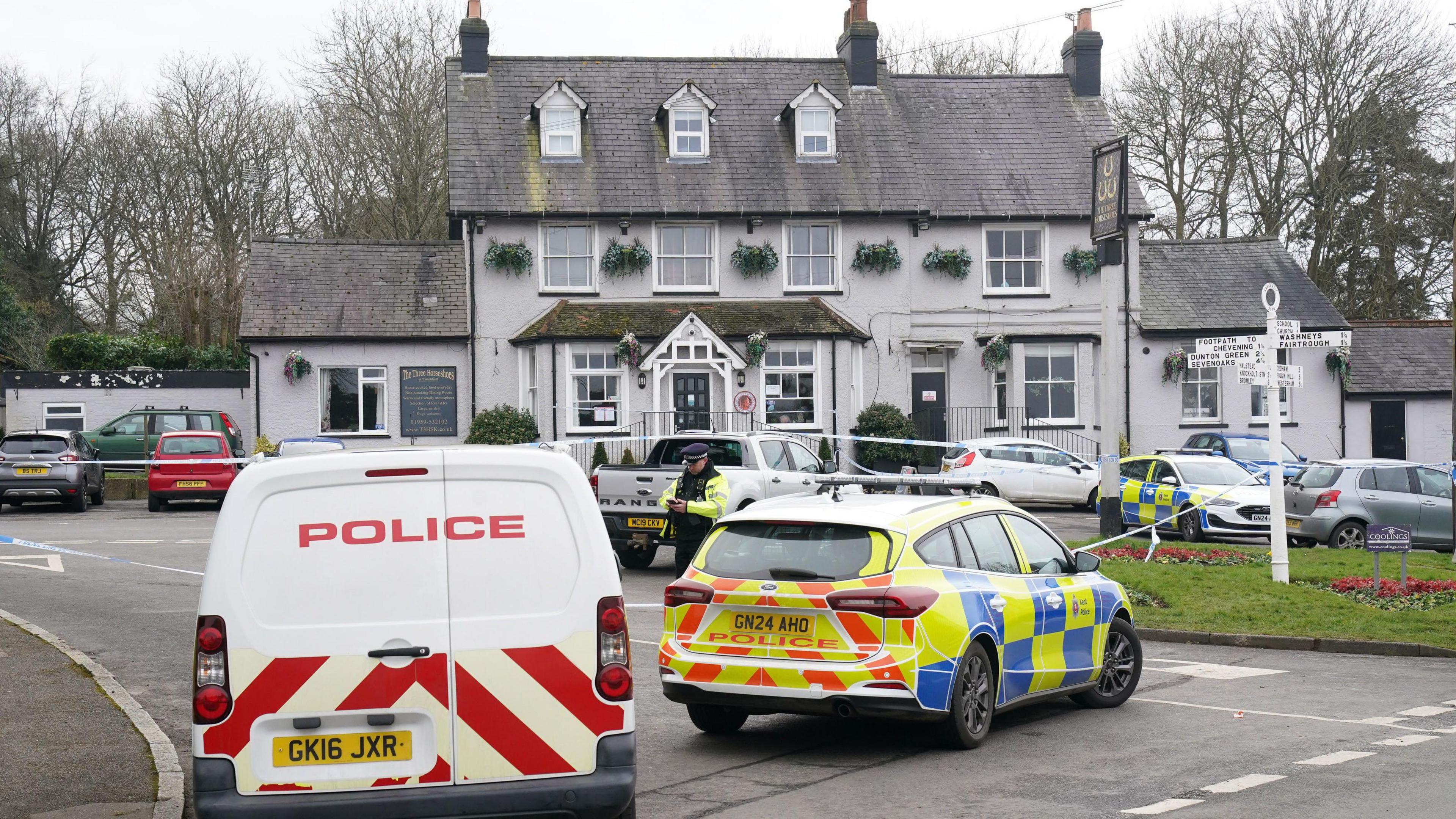 Two police vehicles are parked outside a white pub. 