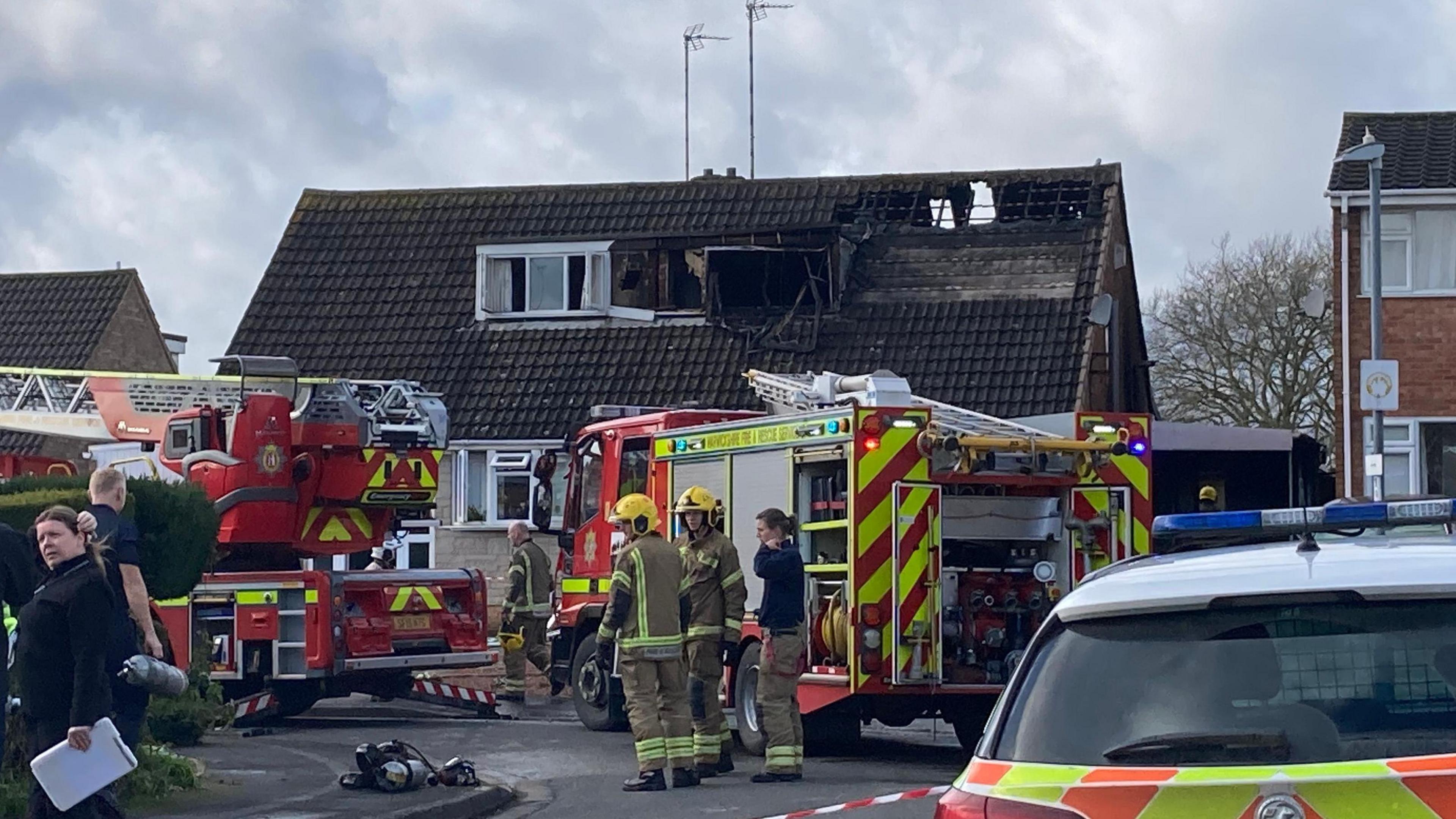 A semi-detached two-storey house with severe fire damage with firefighters and fire engines in front next to police cars