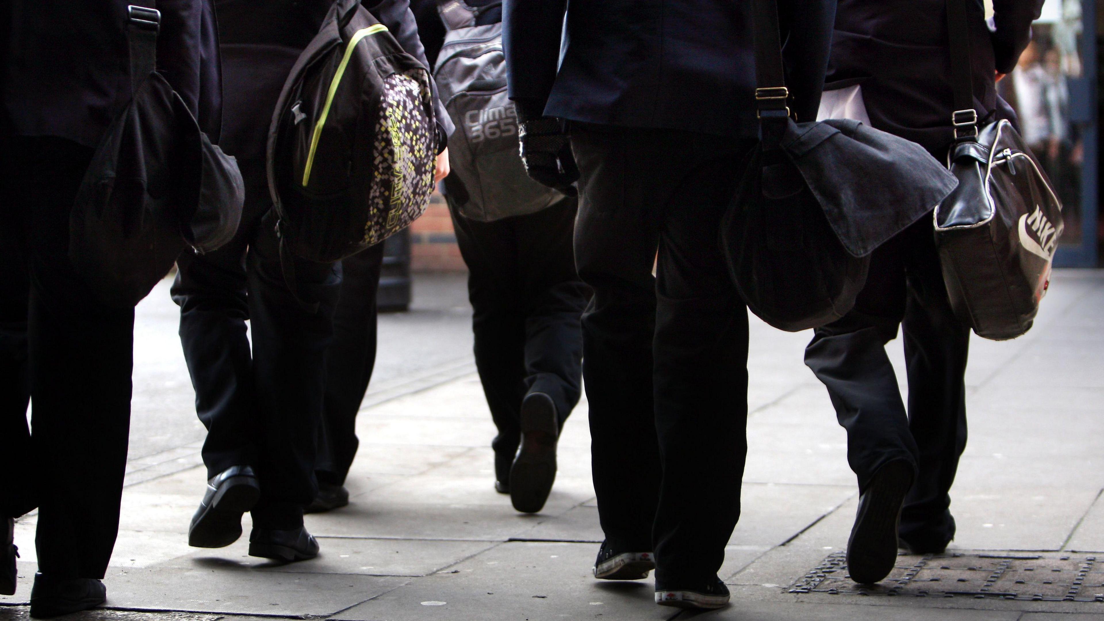 Behind a group of young people walking with school bags. 