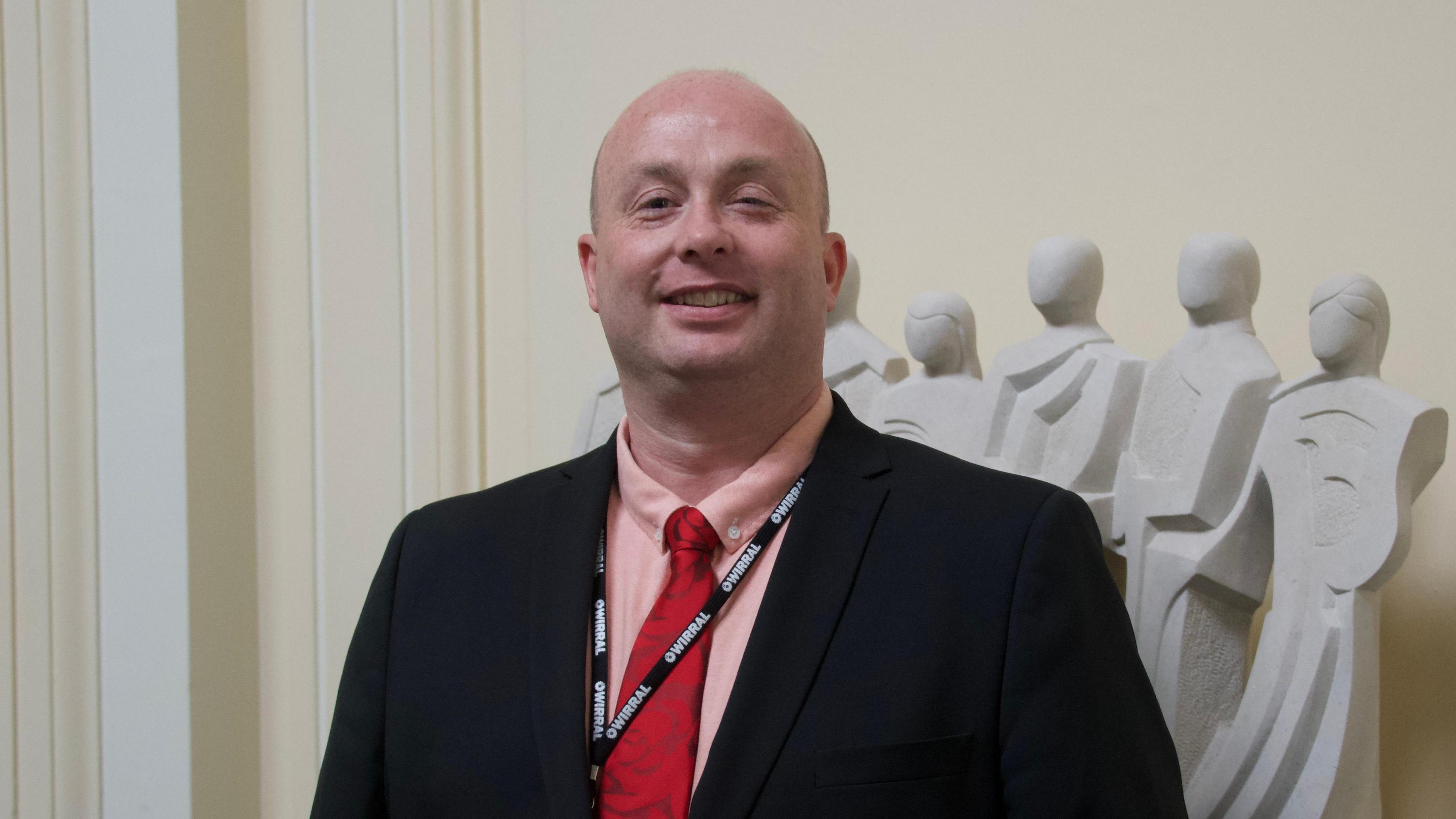 Councillor Paul Stuart. He is smiling, has no hair, and is wearing a black jacket, pink shirt, and red tie.