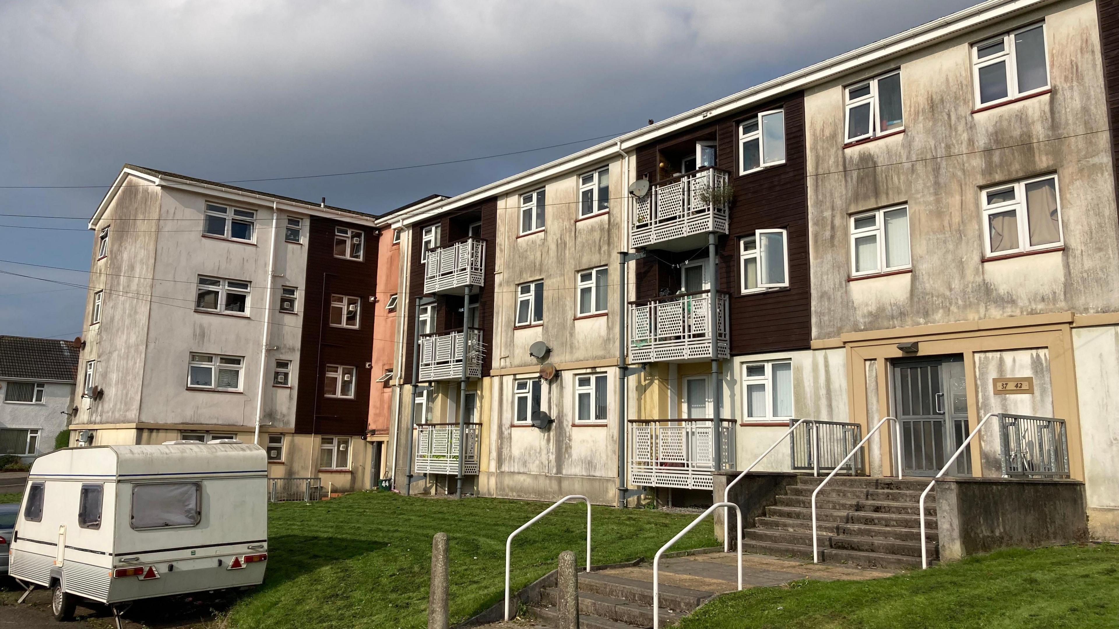 an old caravan parked outside a dilapidated block of flats