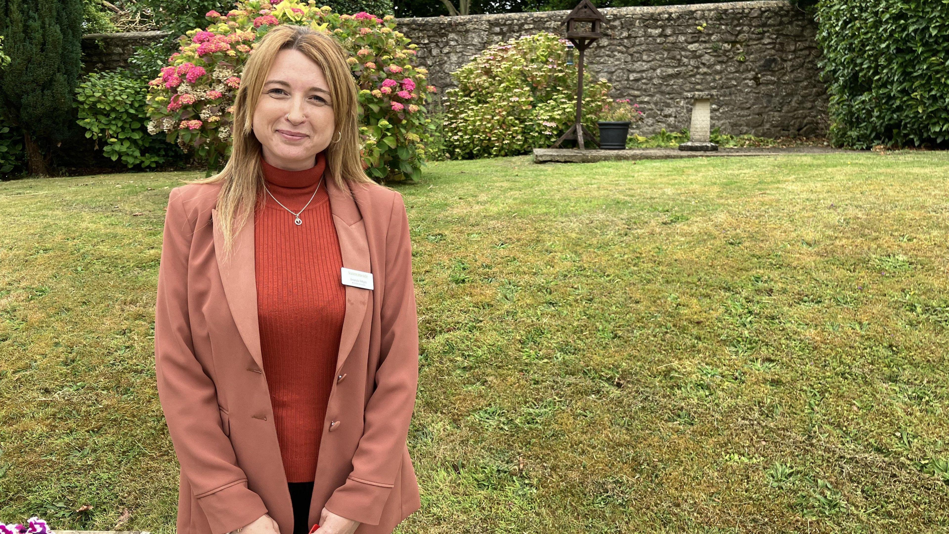 Amanda Whyte stood in the garden outside the care home, backed by flowers and a grassy hill