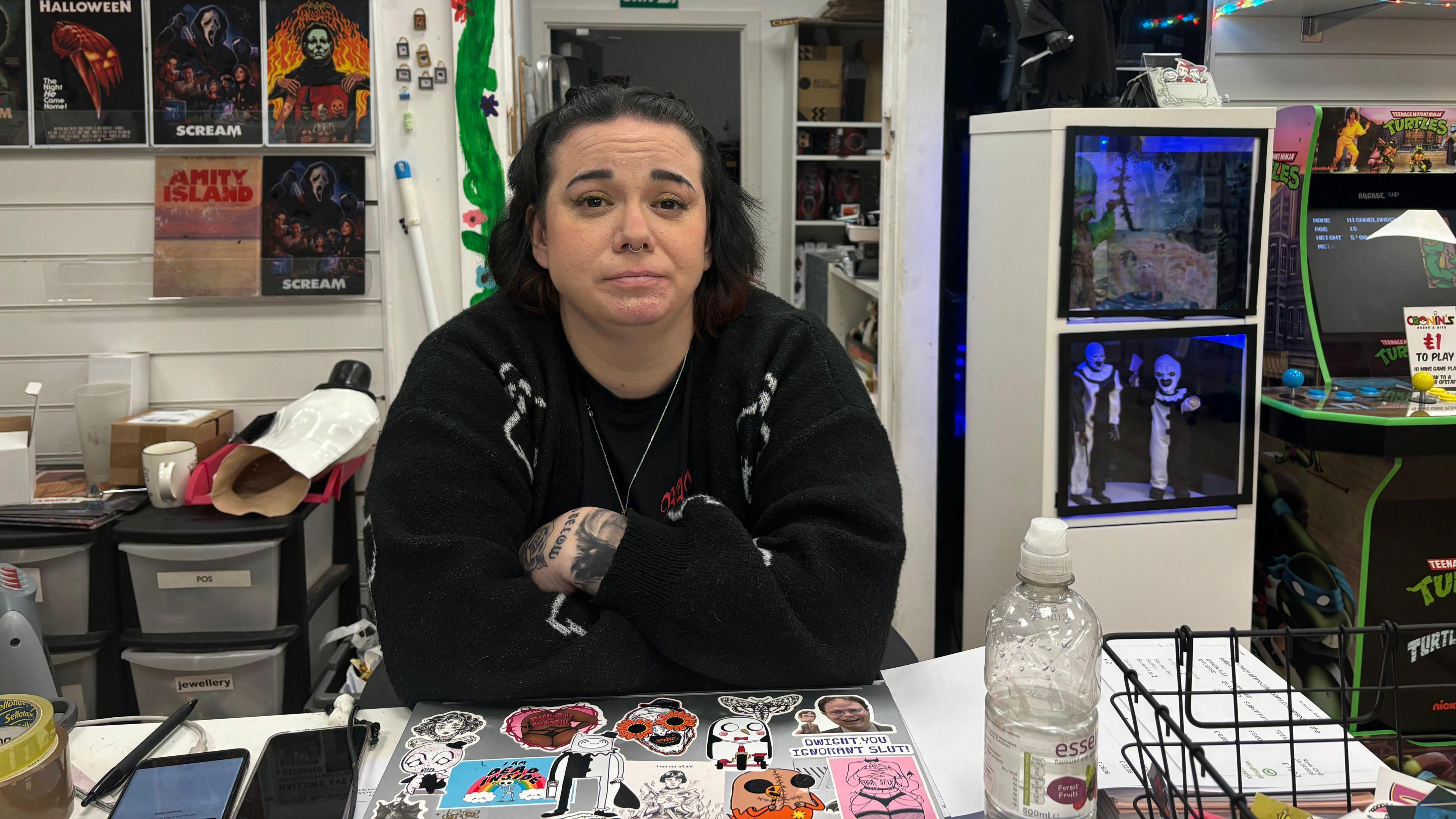 Lianne Cronin dressed in black standing with arms crossed behind a shop counter