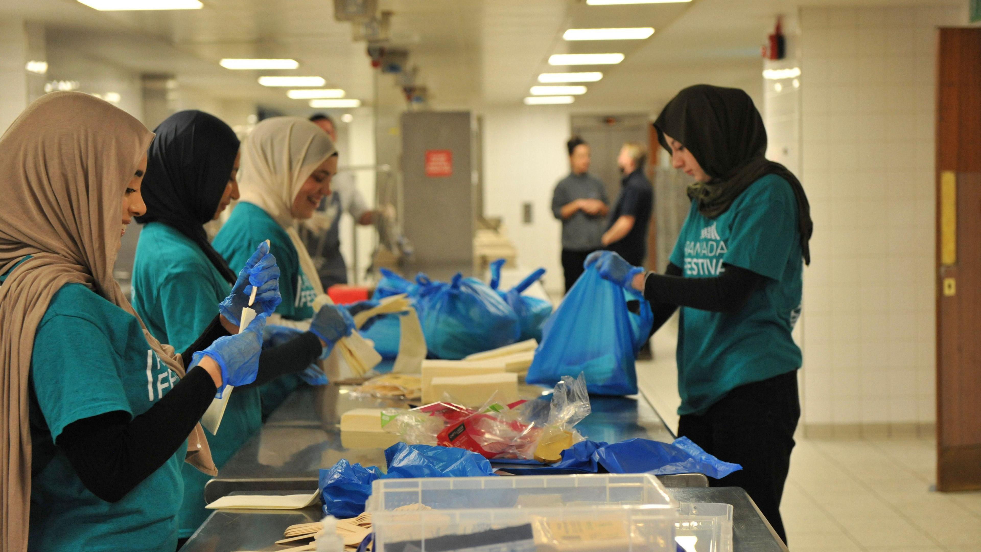 Charity volunteers wearing blue t-shirts and headscarves preparing food bags 