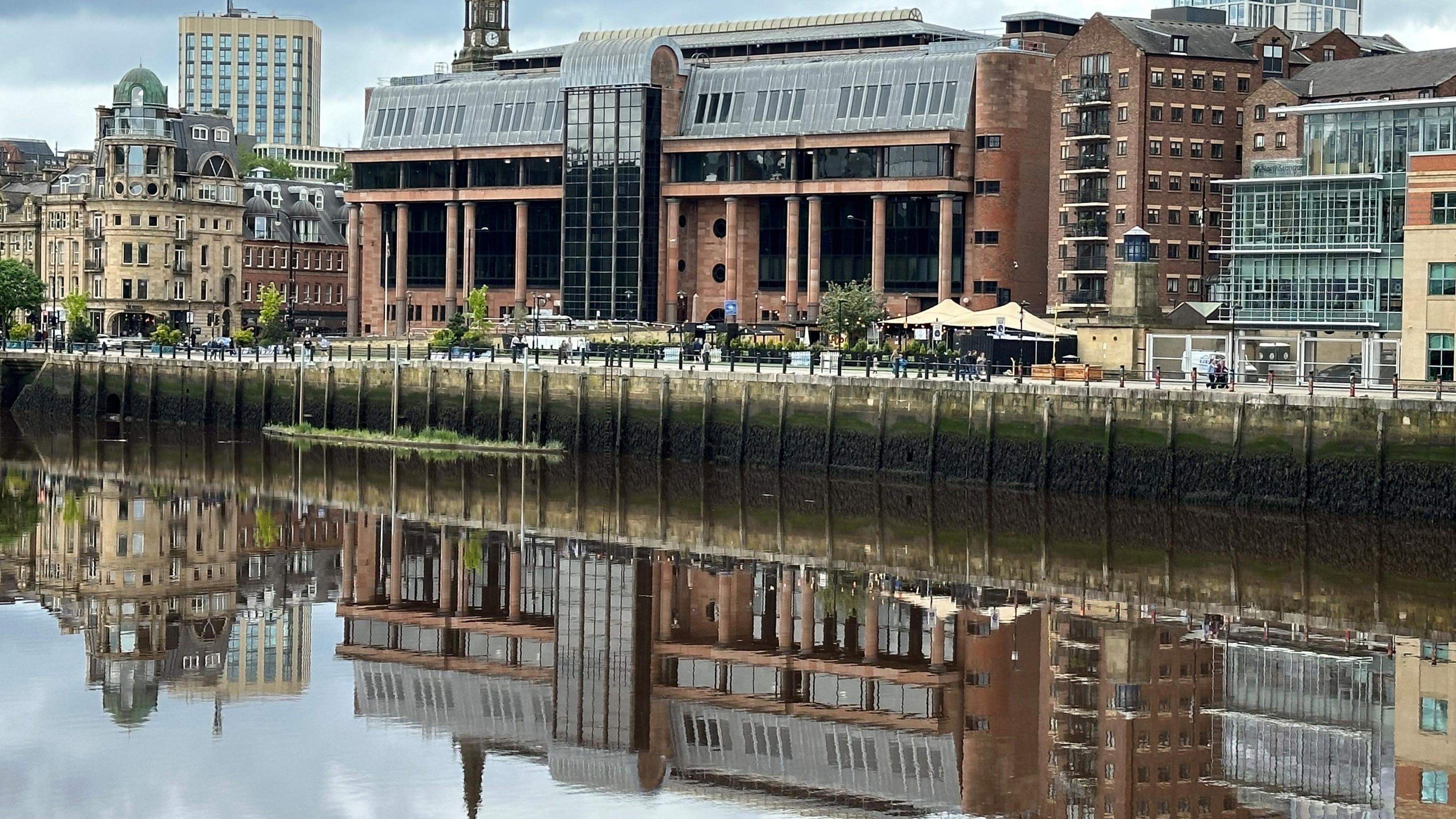 A large red court building reflected in a river running in front of it