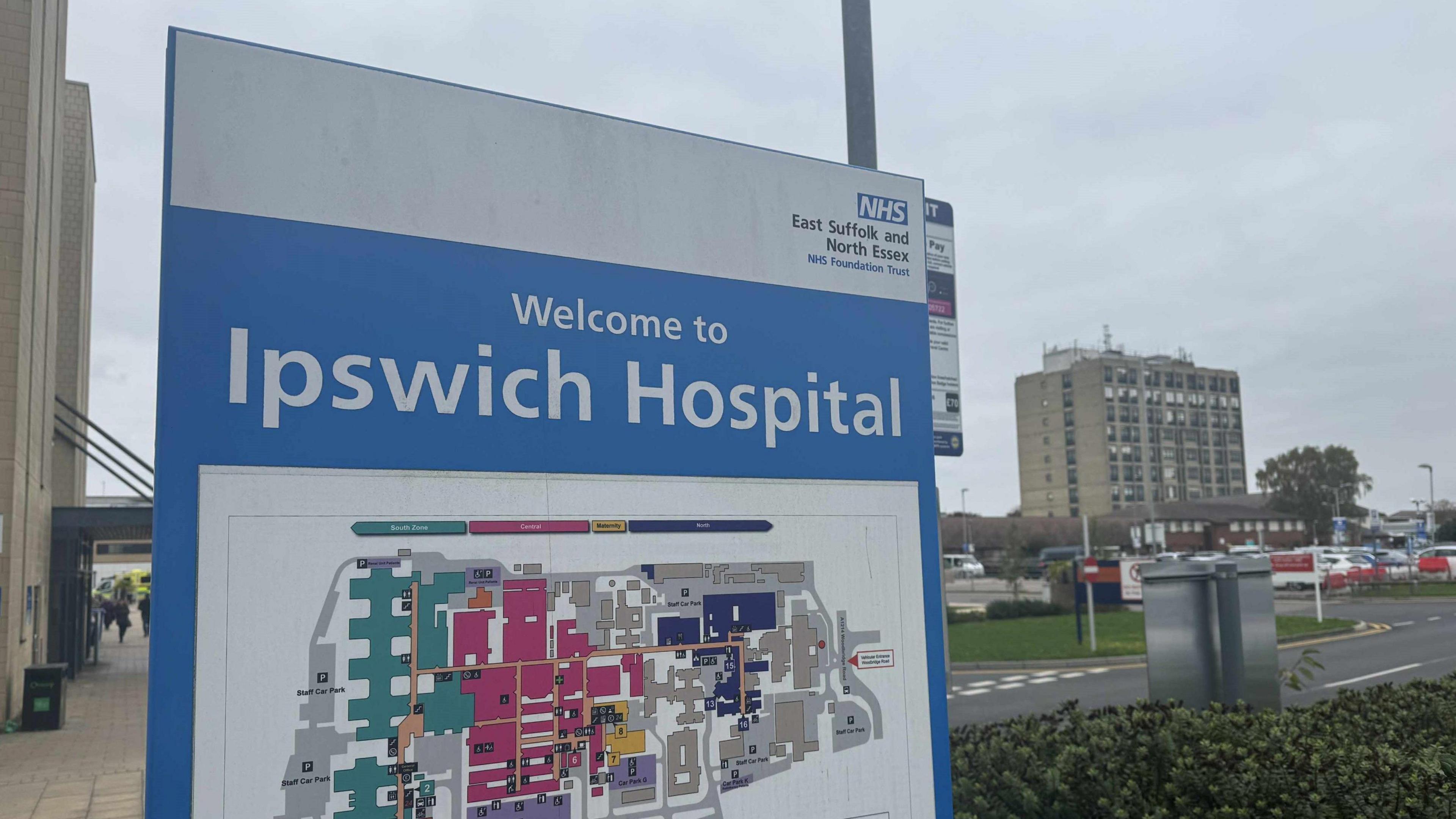 A Welcome to Ipswich Hospital sign with a map of the hospital on it. A large hospital building is in the background.